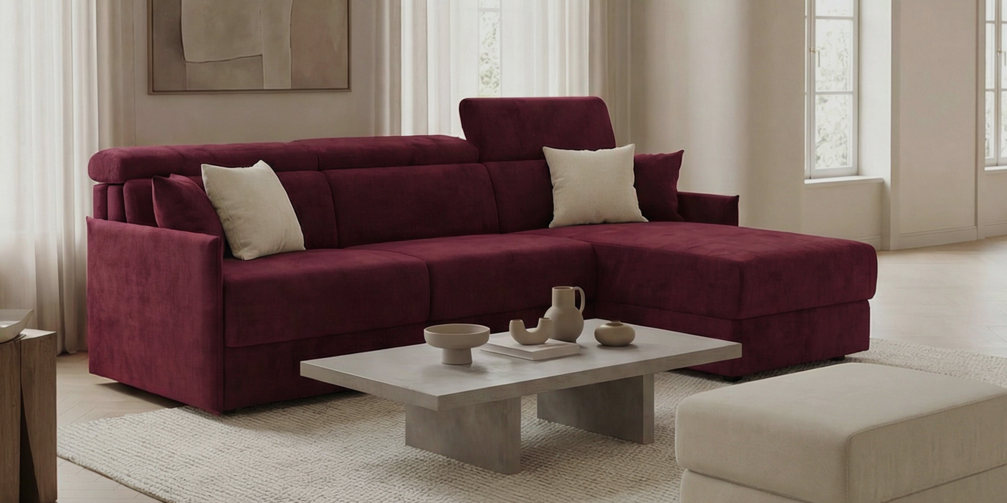 Un soggiorno moderno con divano componibile bordeaux, tavolino da caffè in legno chiaro, tende beige, opere d'arte astratte e arredamento minimalista in toni neutri, inondato di luce naturale dalle alte finestre.