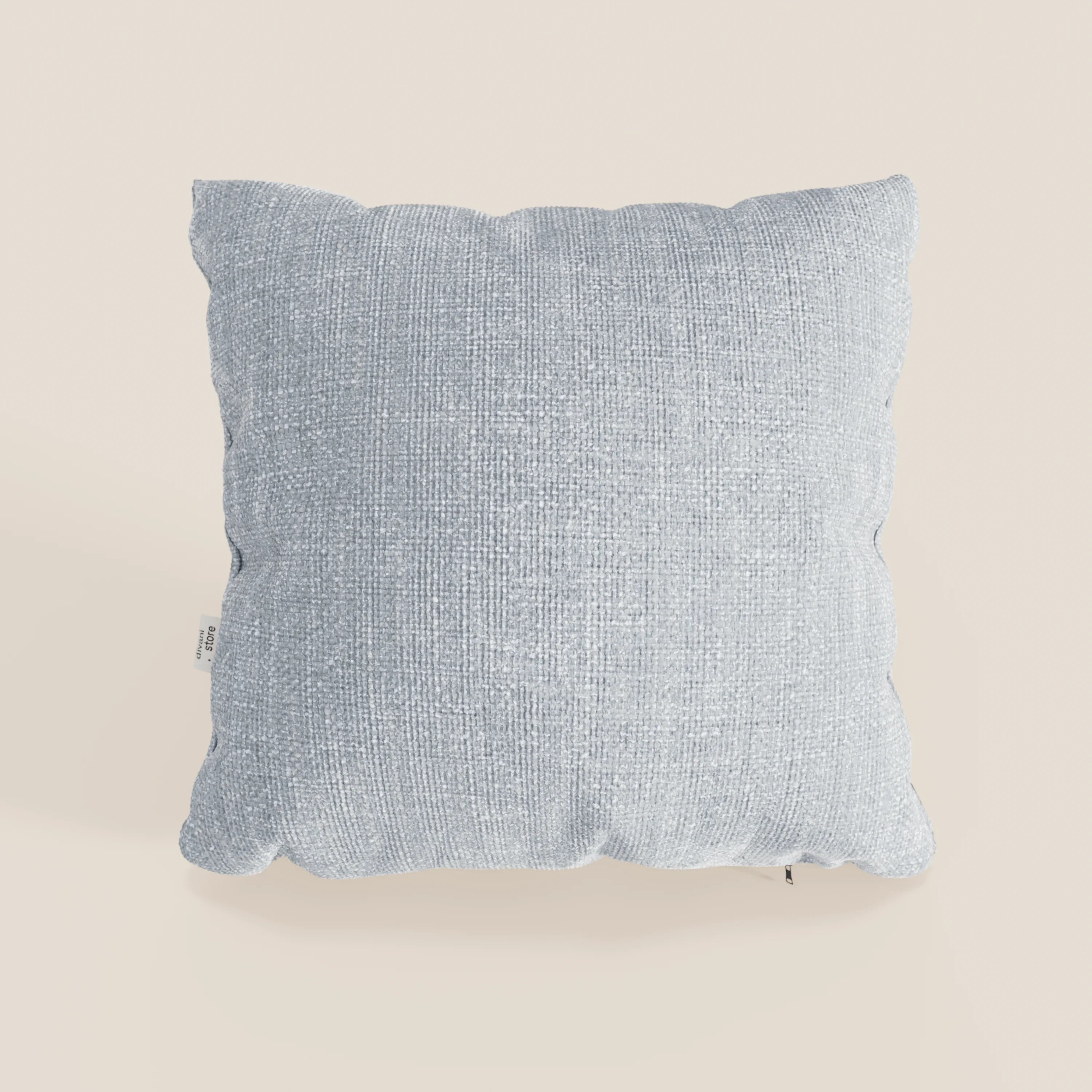Il cuscino Lyon di Divani.Store, 45x45 cm in T06 ghiaccio azzurro, è caratterizzato da un tessuto morbido intrecciato impermeabile e da una piccola targhetta bianca sul bordo sinistro, su un semplice sfondo bianco sporco.