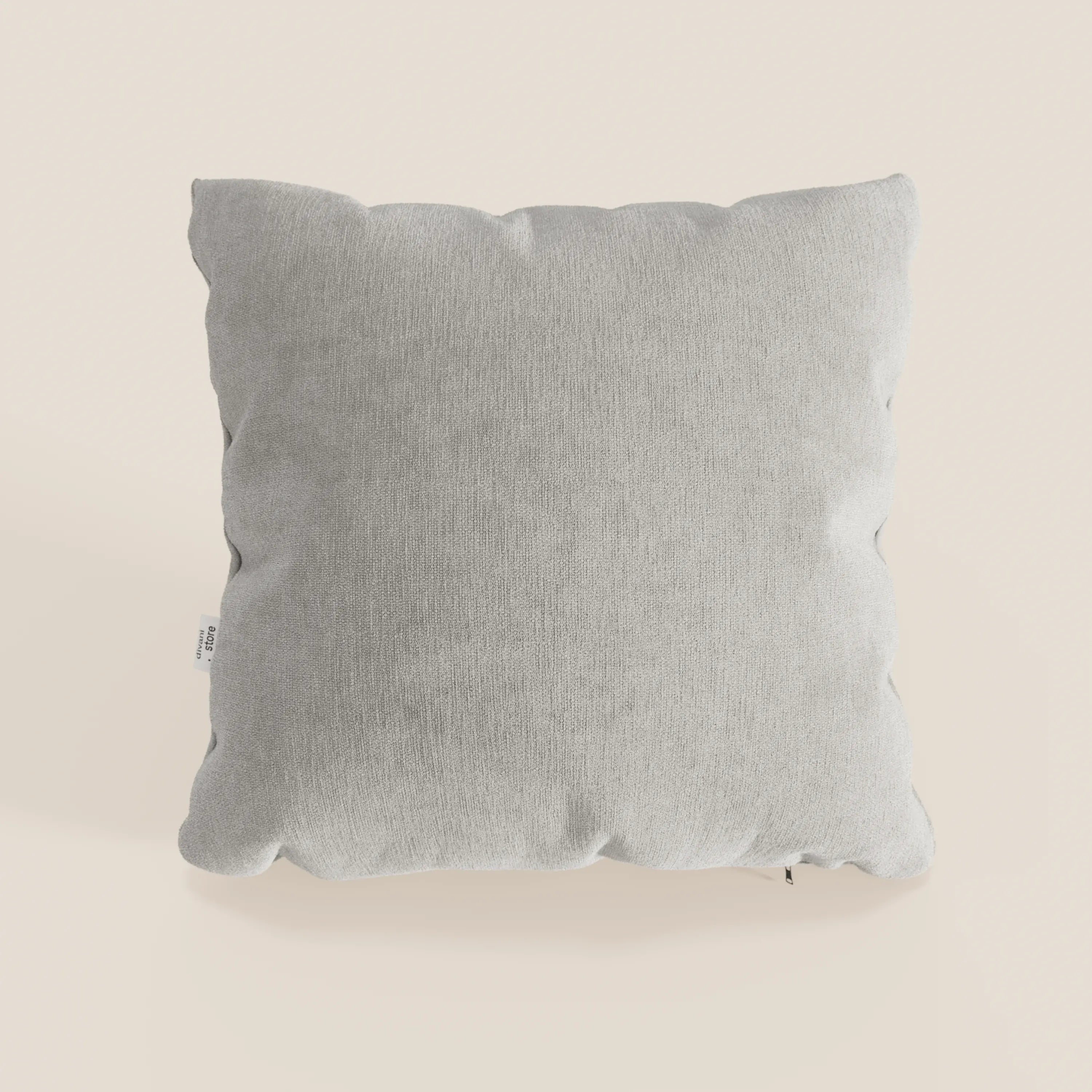 Un cuscino Bolero quadrato grigio chiaro di Divani.Store si trova su uno sfondo beige chiaro. Realizzato in morbido tessuto T31 antimacchia, impermeabile e non restringente, presenta angoli leggermente arrotondati e una piccola etichetta in tessuto sul lato sinistro.