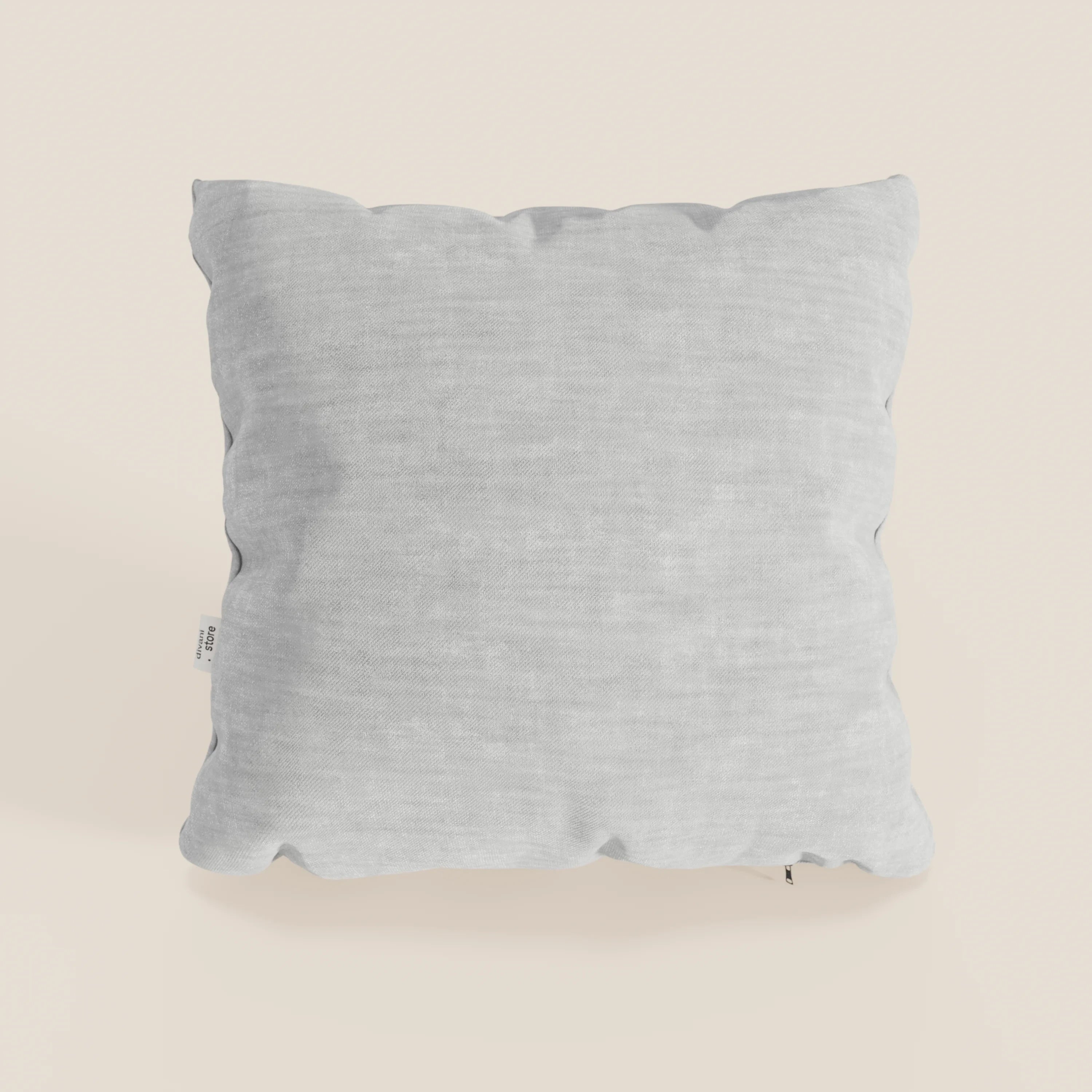 Un cuscino Sofia quadrato grigio chiaro di Divani.Store in morbido velluto nuvolato Easy Clean T35, antimacchia e impermeabile, poggia su un fondo crema chiaro; è morbido, leggermente gonfio, con un'etichetta in tessuto bianco sul bordo sinistro.