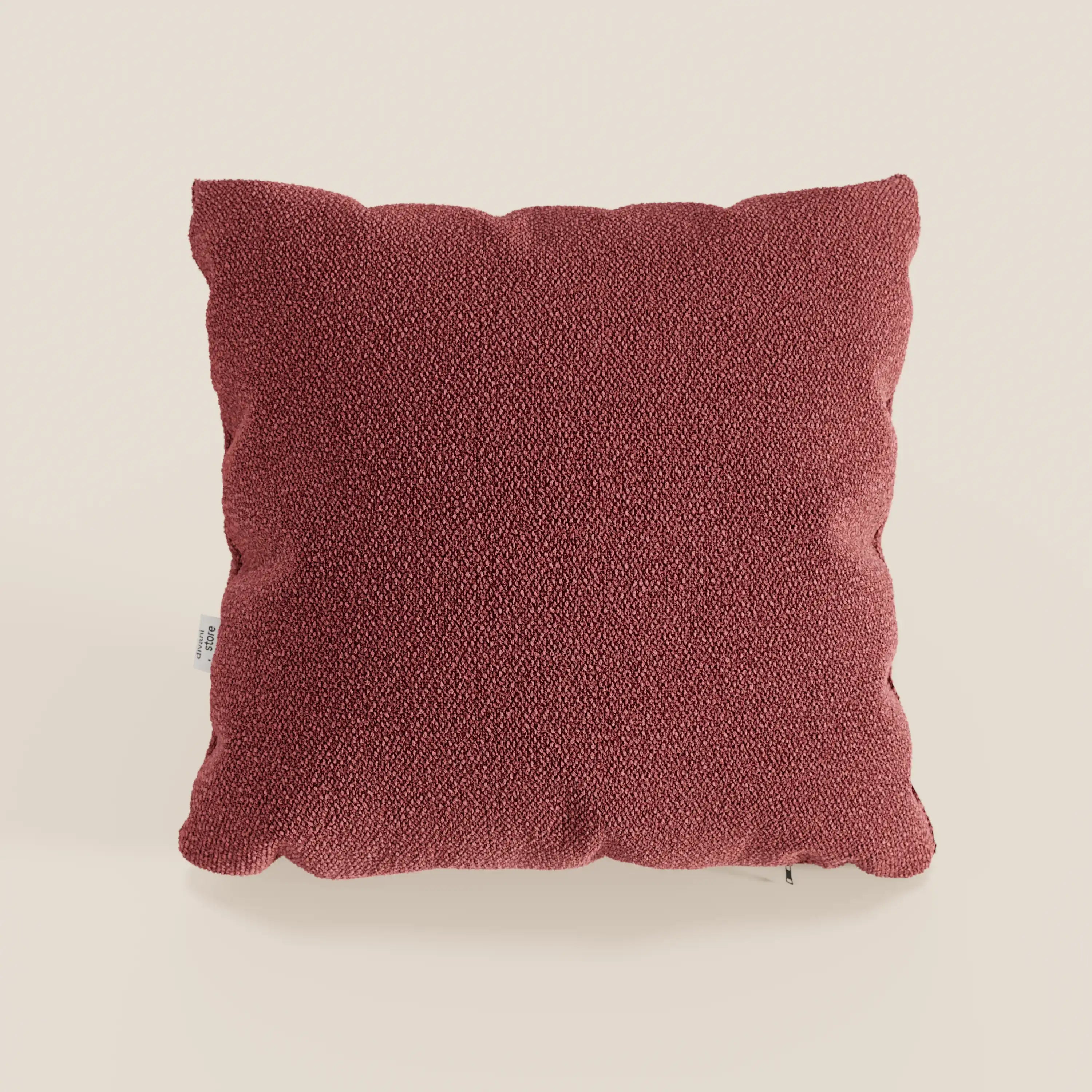 Il cuscino quadrato Lambada di Divani.Store, di colore rosso intenso e realizzato in fresco tessuto simil-cotone impermeabile e antimacchia (T33), è posto al centro di un semplice sfondo beige. Ha un aspetto felpato, con angoli arrotondati e una piccola etichetta sulla sinistra.
