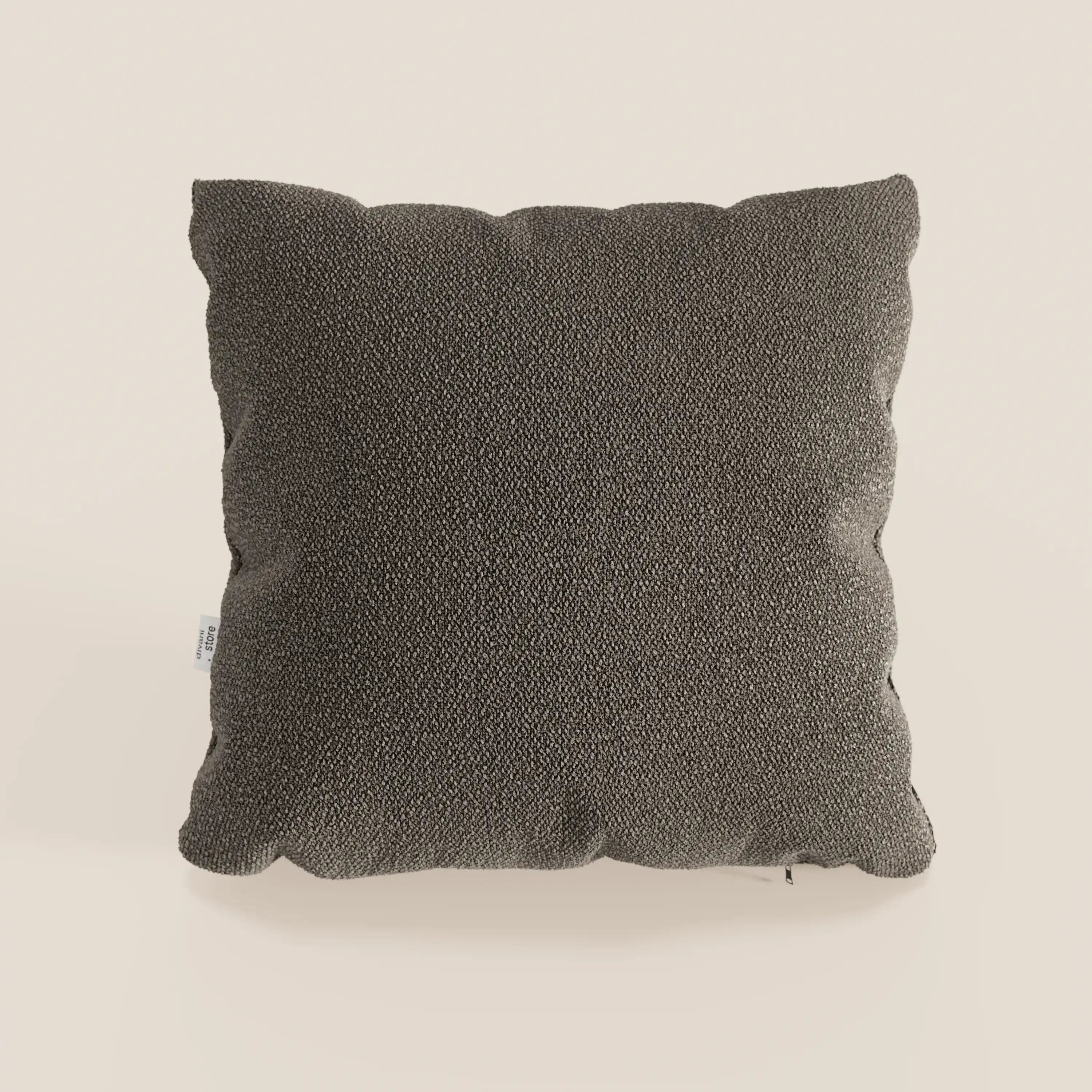 Un cuscino singolo Lambada grigio scuro di Divani.Store, realizzato in tessuto fresco, antimacchia e impermeabile tipo cotone T33, è presentato con bordi felpati e un'etichetta laterale bianca su uno sfondo beige chiaro. Il design è semplice e moderno.