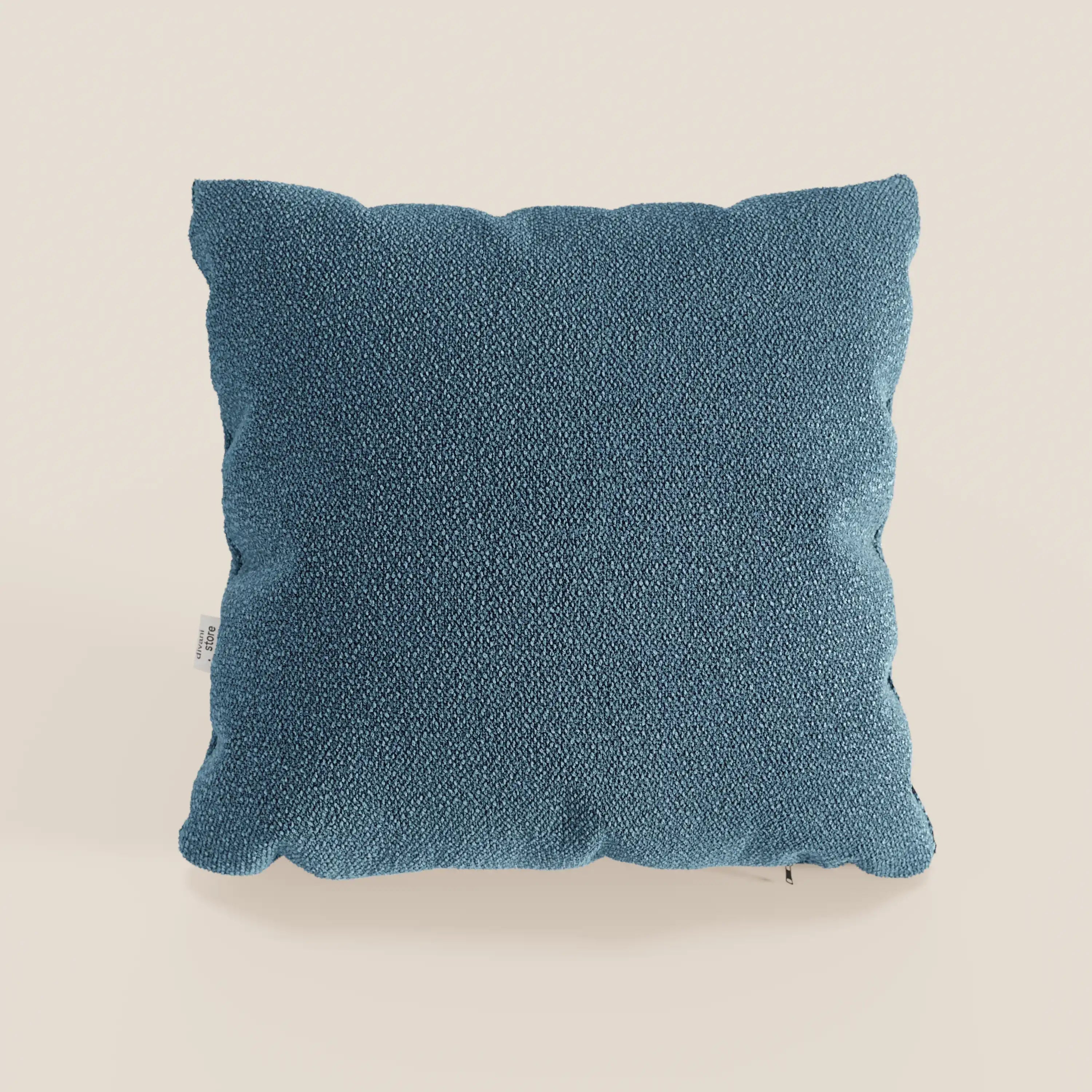 Il cuscino Lambada di Divani.Store è un cuscino quadrato blu in tessuto simil-cotone smacchiabile e impermeabile T33, caratterizzato da una superficie morbida e strutturata e da una piccola etichetta bianca sulla sinistra, su uno sfondo beige chiaro.