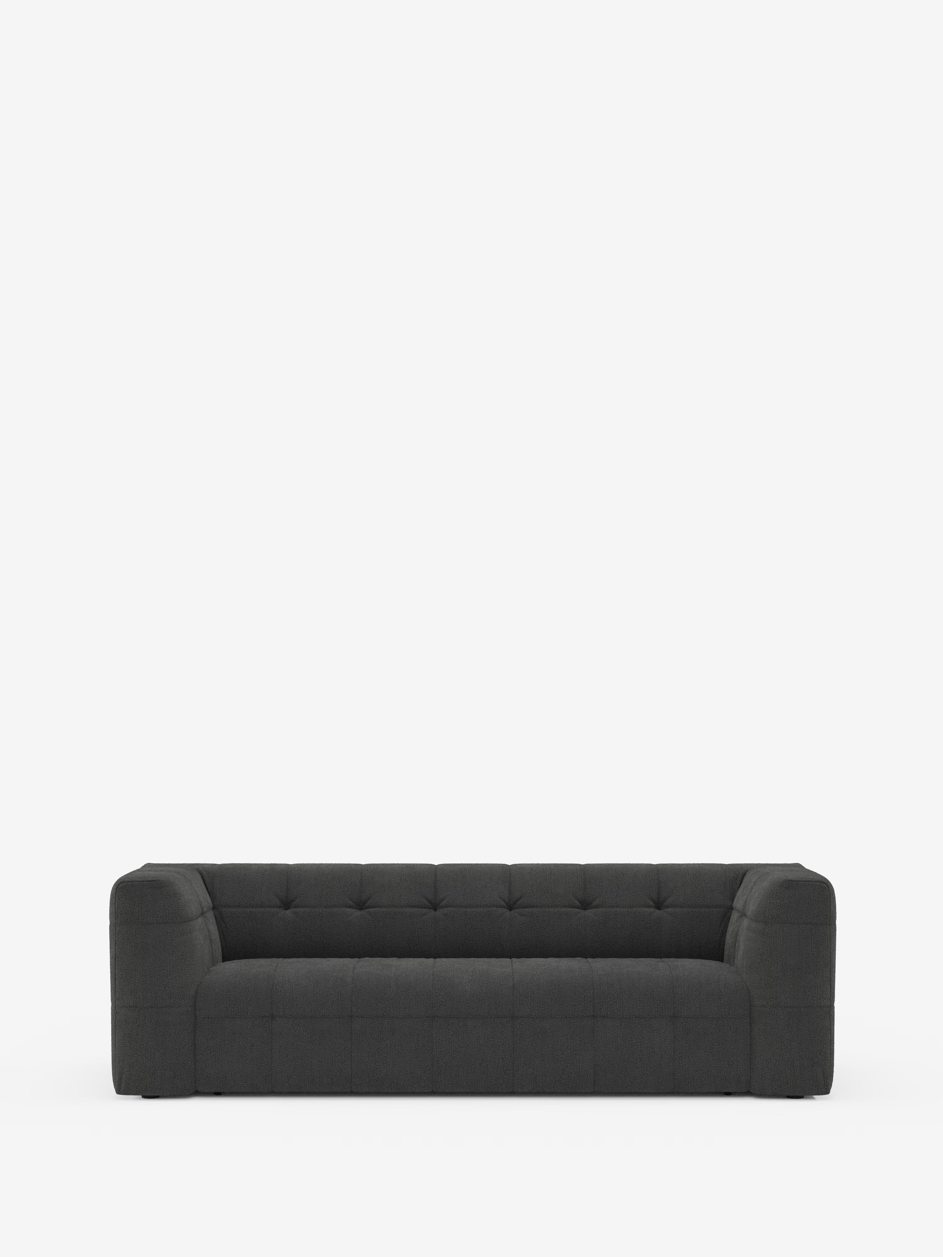 Un moderno divano modulare Mosaic Divano a 3 e 4 posti, di colore grigio scuro, realizzato in bouclé da Divani.Store, caratterizzato da un design capitonné con braccioli squadrati e schienale basso, è posizionato al centro su uno sfondo bianco a tinta unita. Il divano, morbido e trapuntato, presenta cuciture a vista e offre ampio spazio per tre persone.