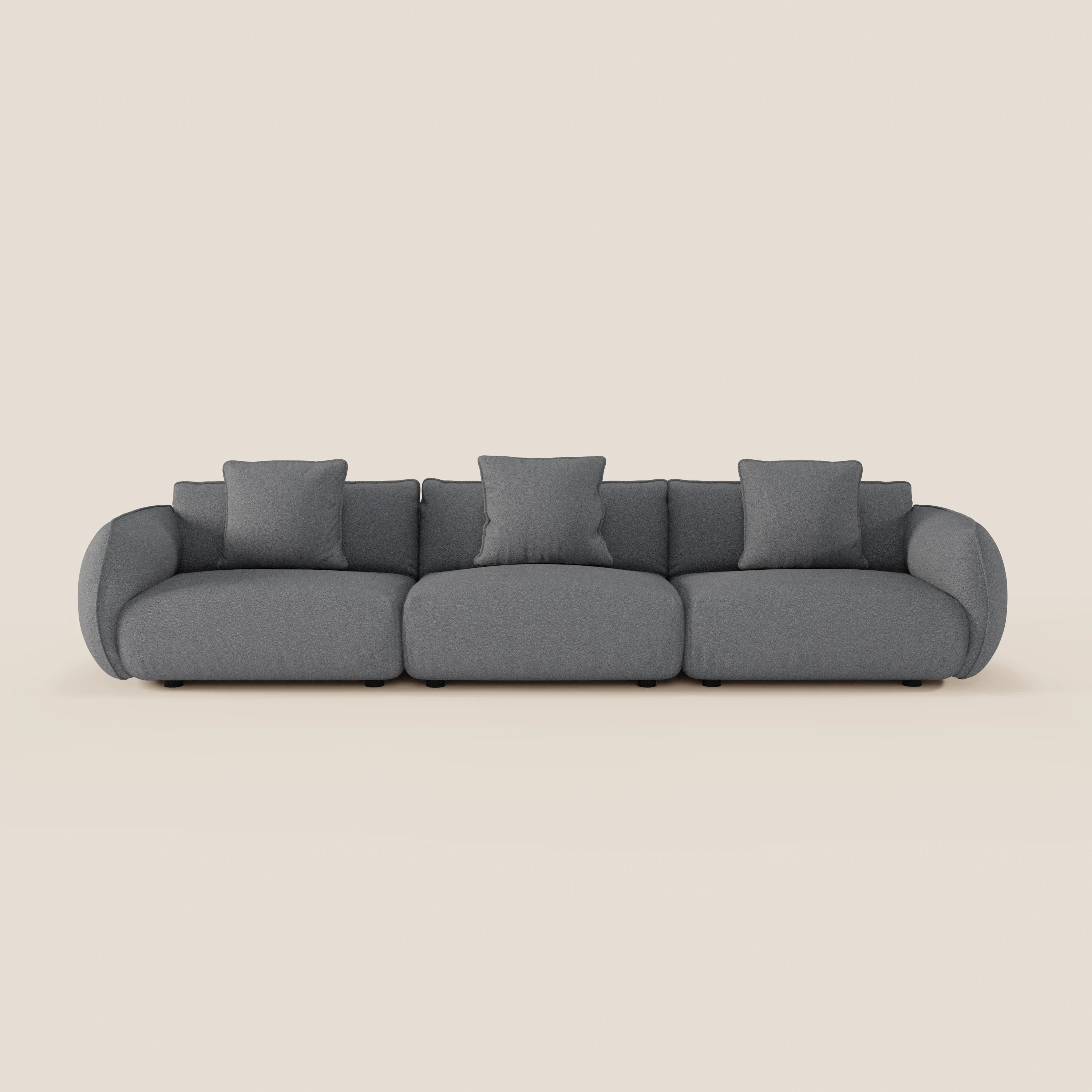 Il divano Nimbus modulare a 3 sedute di Divani.Store, in morbido tessuto smacchiabile effetto cotone T33 colore grigio scuro, ha braccioli e schienale arrotondati, tre cuscini di seduta e quattro cuscini quadrati, su sfondo beige chiaro.