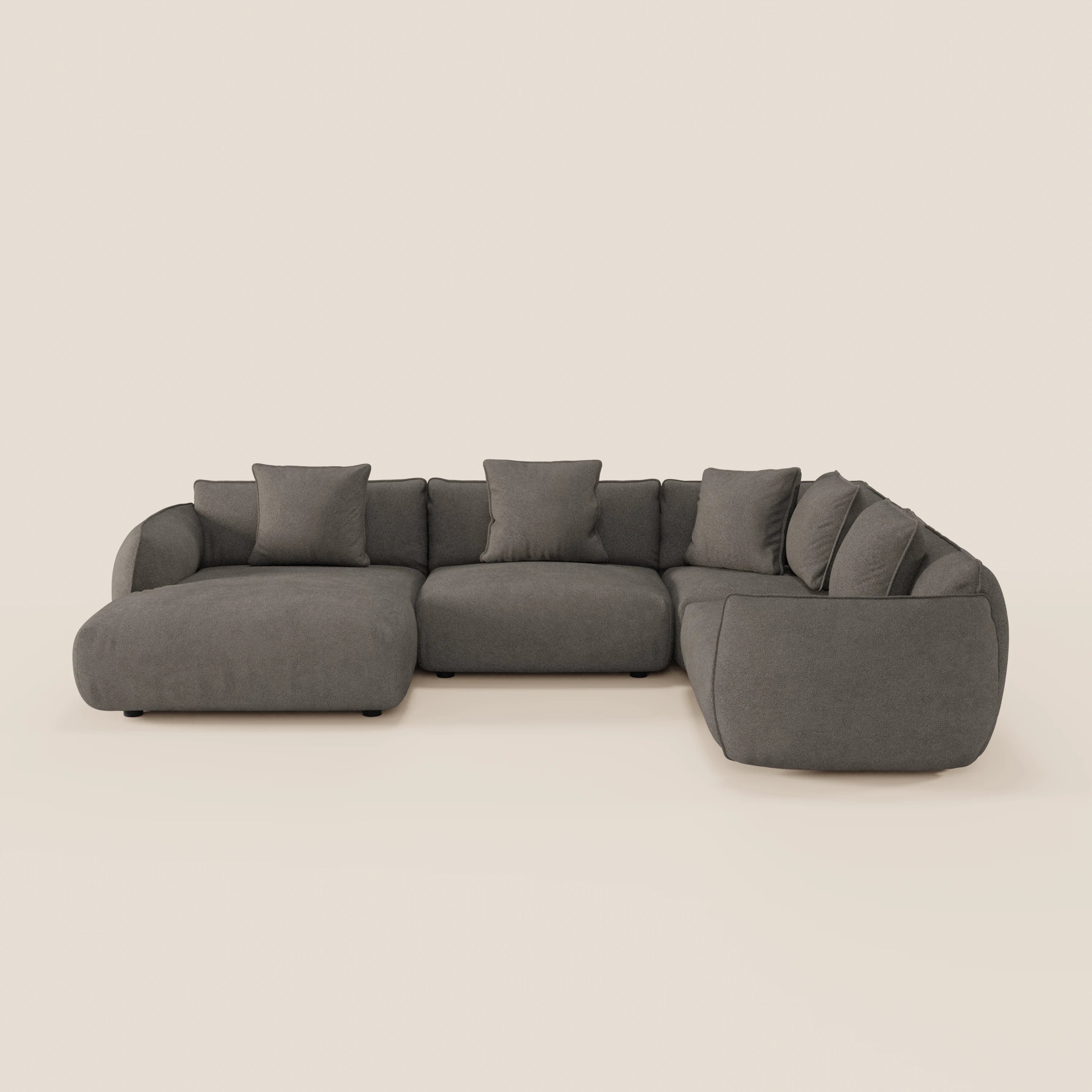 Il divano angolare panoramico componibile Nimbus di Divani.Store, in tessuto antimacchia grigio scuro, presenta bordi arrotondati, cinque cuscini coordinati e un design ad angolo retto per un'ampia seduta e un look minimalista e contemporaneo.