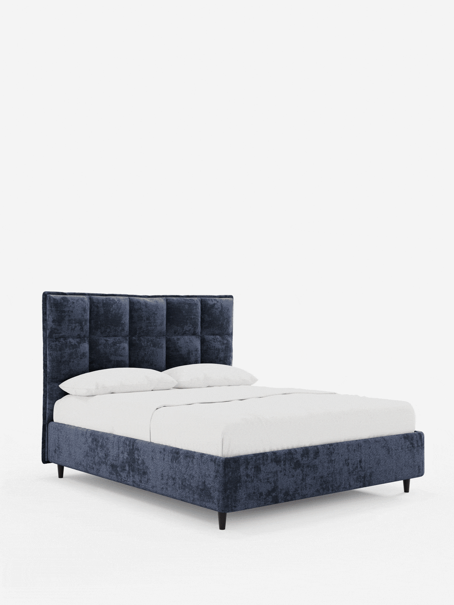 Il letto imbottito AURO con contenitore e testiera alta capitonné in ciniglia Oeko-Tex® è un letto imbottito blu navy con una testiera alta capitonné, rivestito con lenzuola bianche, su semplici gambe scure su uno sfondo a tinta unita.