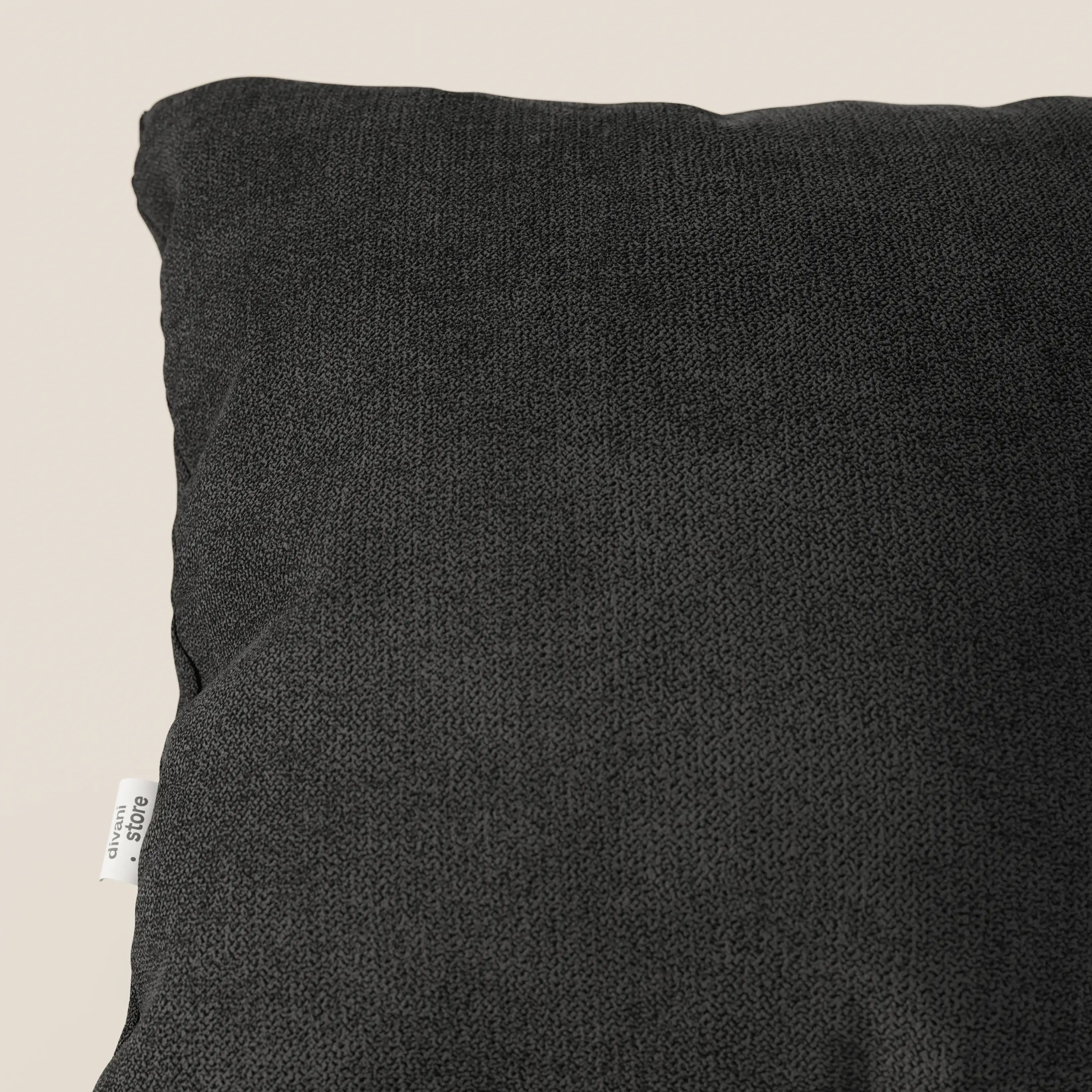 Primo piano del cuscino Destiny 45x45 cm in tessuto morbido impermeabile T02 nero di Divani.Store, su uno sfondo beige chiaro. Sul bordo sinistro è presente una piccola etichetta bianca con testo nero e l'angolo superiore sinistro è leggermente rialzato.
