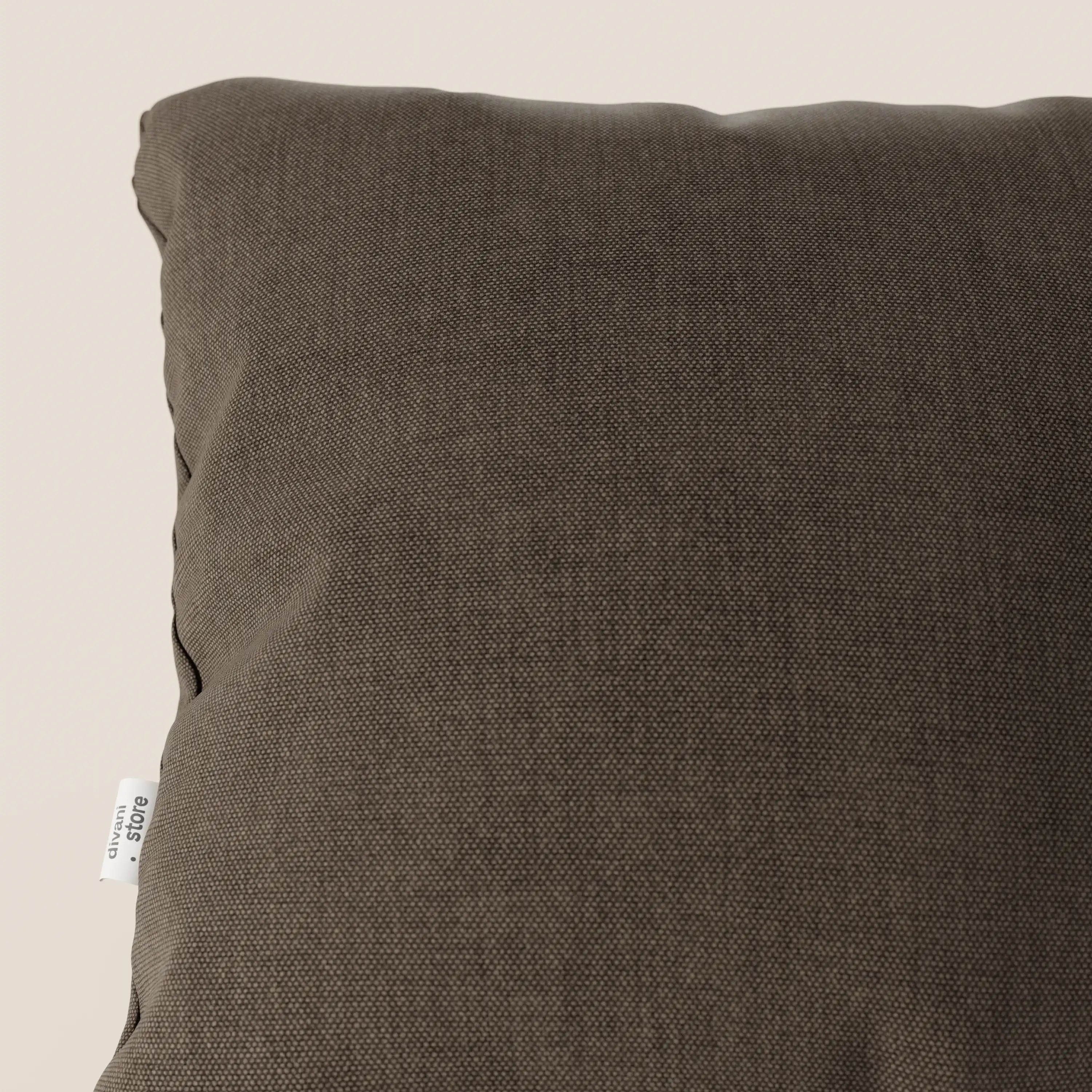Primo piano del cuscino Honey 45x45 cm di Divani.Store in T13 marrone. Realizzato in similcotone impermeabile con una sottile trama, presenta una piccola etichetta bianca sulla cucitura sinistra ed è inserito in uno sfondo beige.