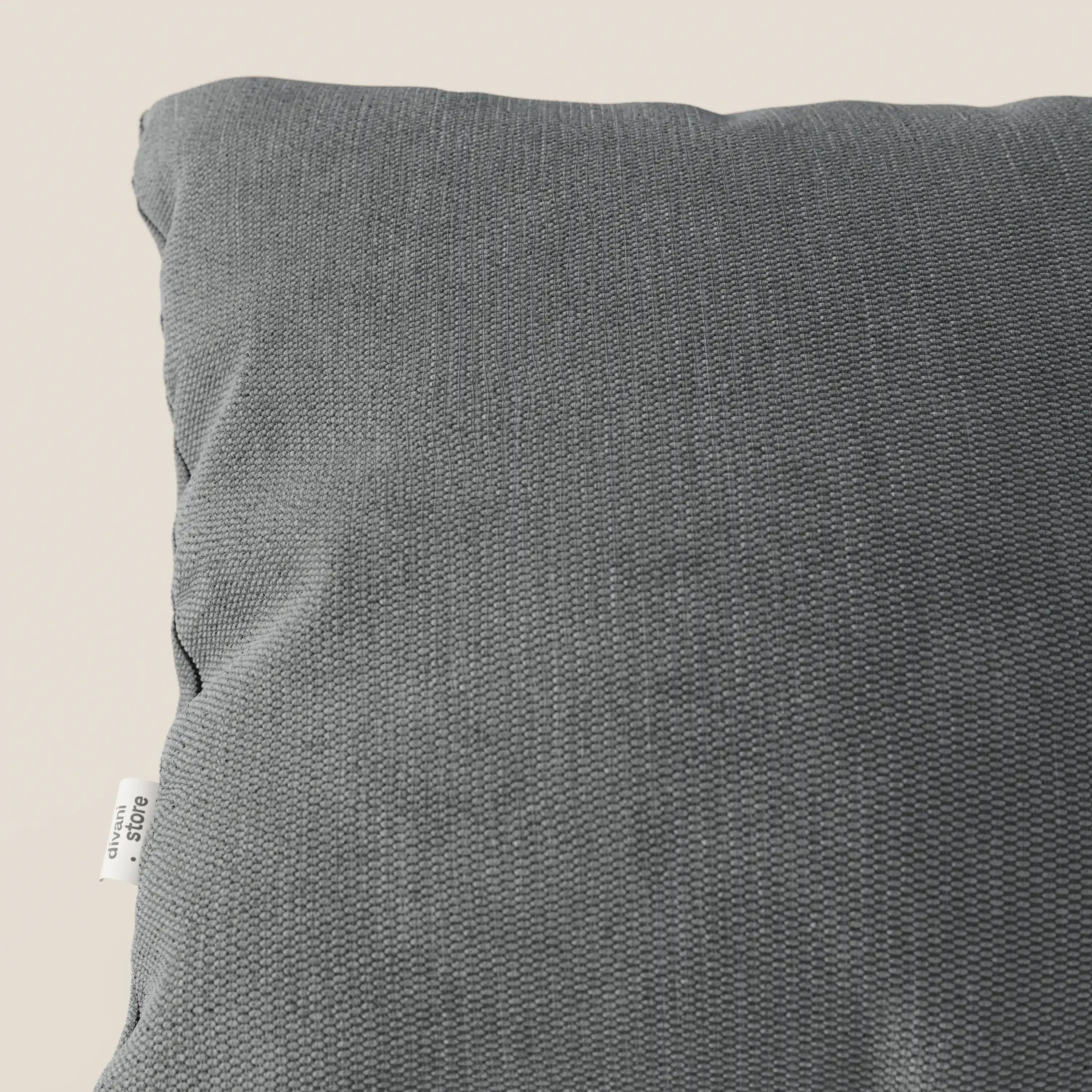 Primo piano del cuscino Miami di Divani.Store in morbido tessuto impermeabile T14 grigio, che mostra l'angolo superiore sinistro con una piccola etichetta bianca sulla cucitura. Lo sfondo è un semplice beige chiaro.