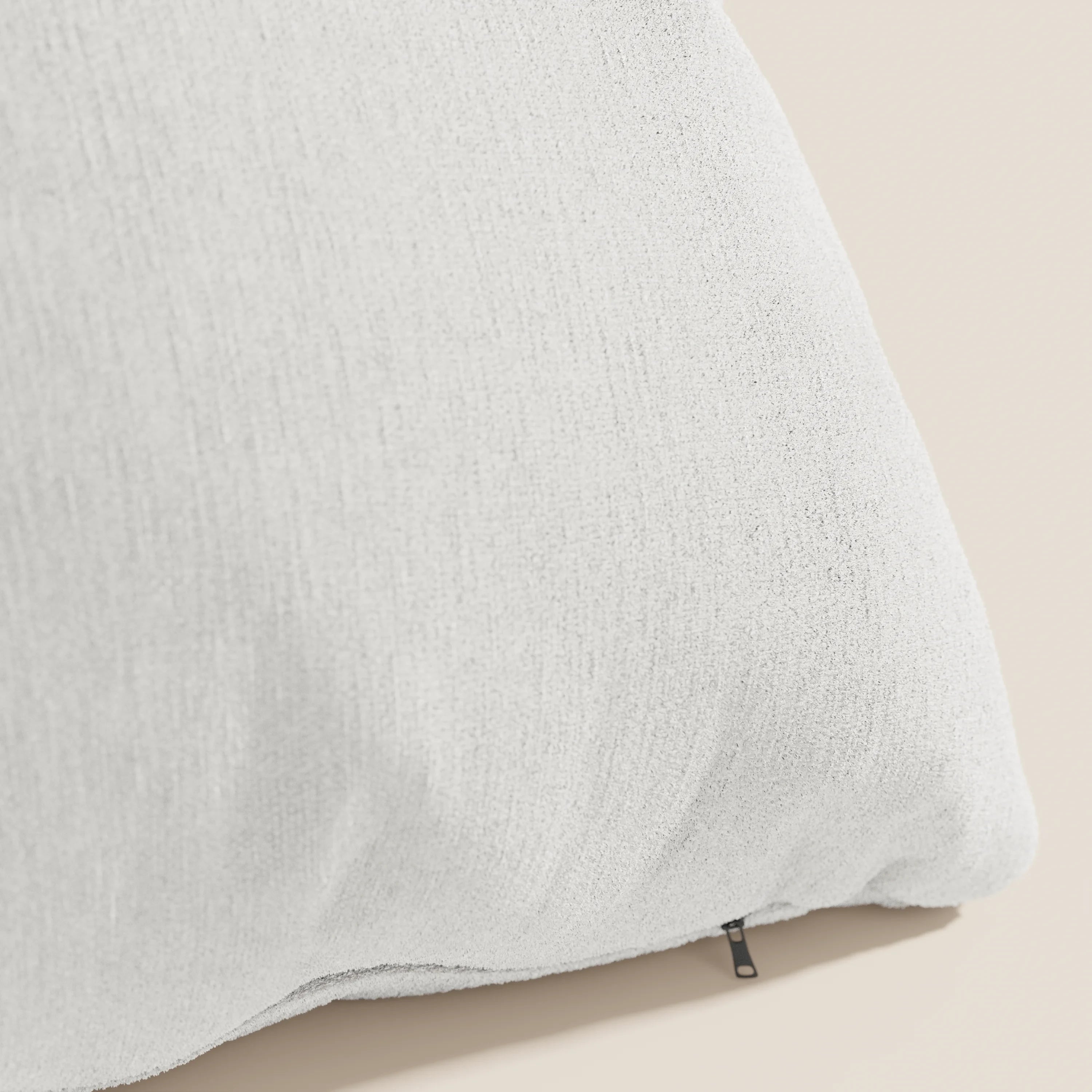 Primo piano dell'angolo di un cuscino Bolero bianco di Divani.Store, realizzato in morbido tessuto T31 antimacchia, impermeabile e non restringente. Una cerniera nera sulla cucitura mostra il rivestimento sfoderabile. Lo sfondo beige ne sottolinea la consistenza.