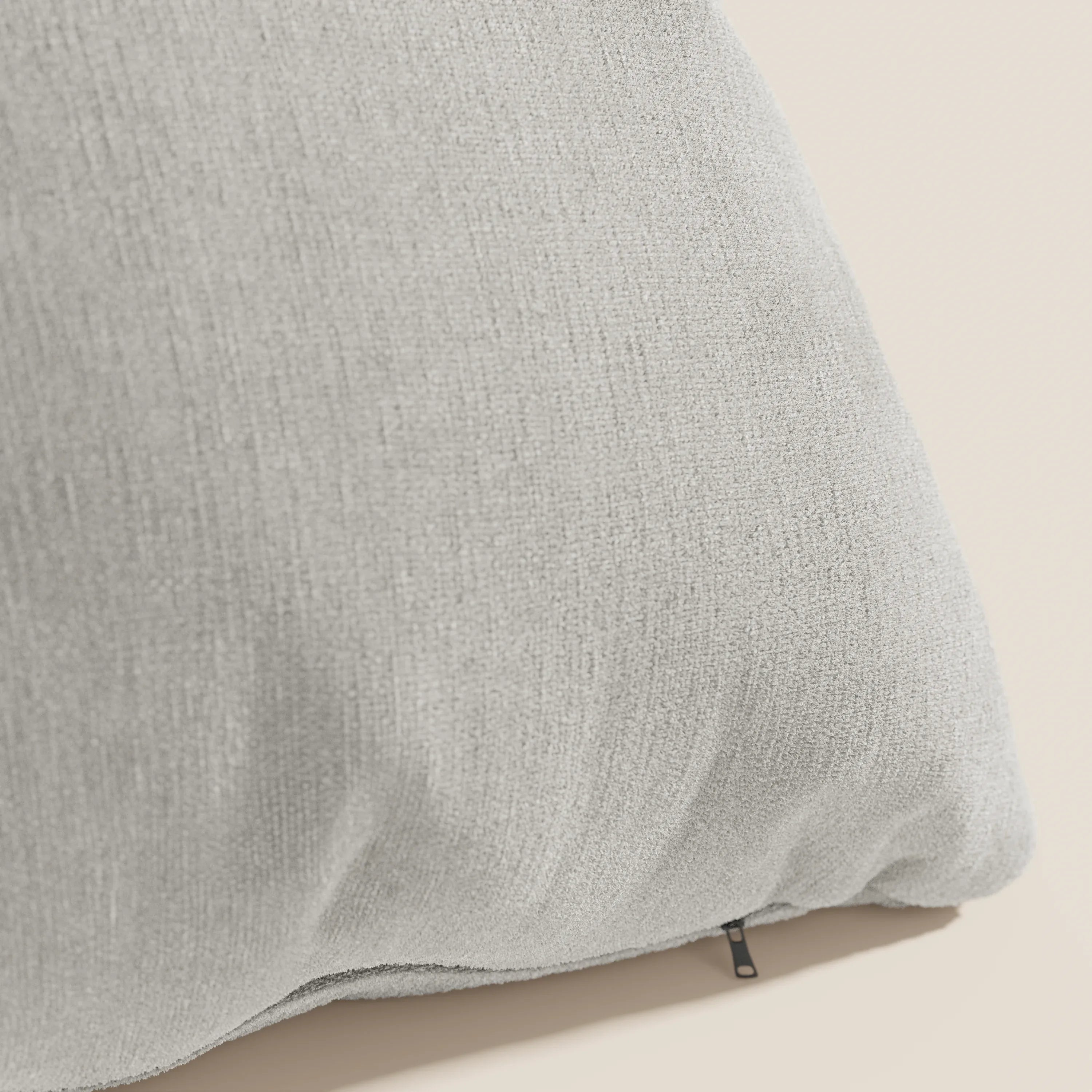 Primo piano del cuscino Bolero di Divani.Store in grigio chiaro, con tessuto T31 morbido, antimacchia, impermeabile e termoretraibile, sfoderabile, su sfondo beige con trama a vista e tirazip nero.