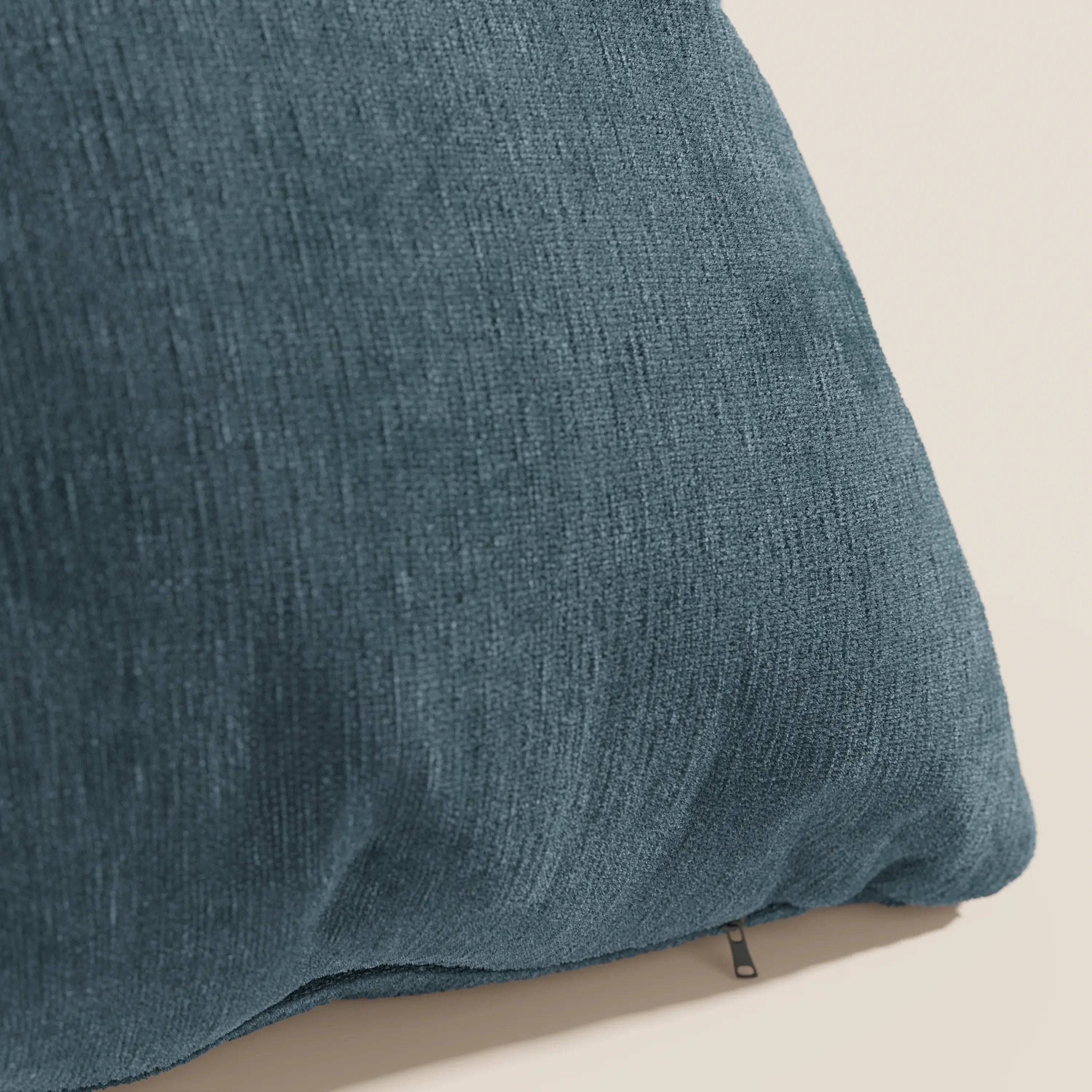 Primo piano di Bolero cuscino di Divani.Store in blu, con tessuto T31 morbido e testurizzato, resistente alle macchie, impermeabile e non restringente. Una piccola cerniera vicino al bordo inferiore aggiunge un dettaglio sullo sfondo chiaro.