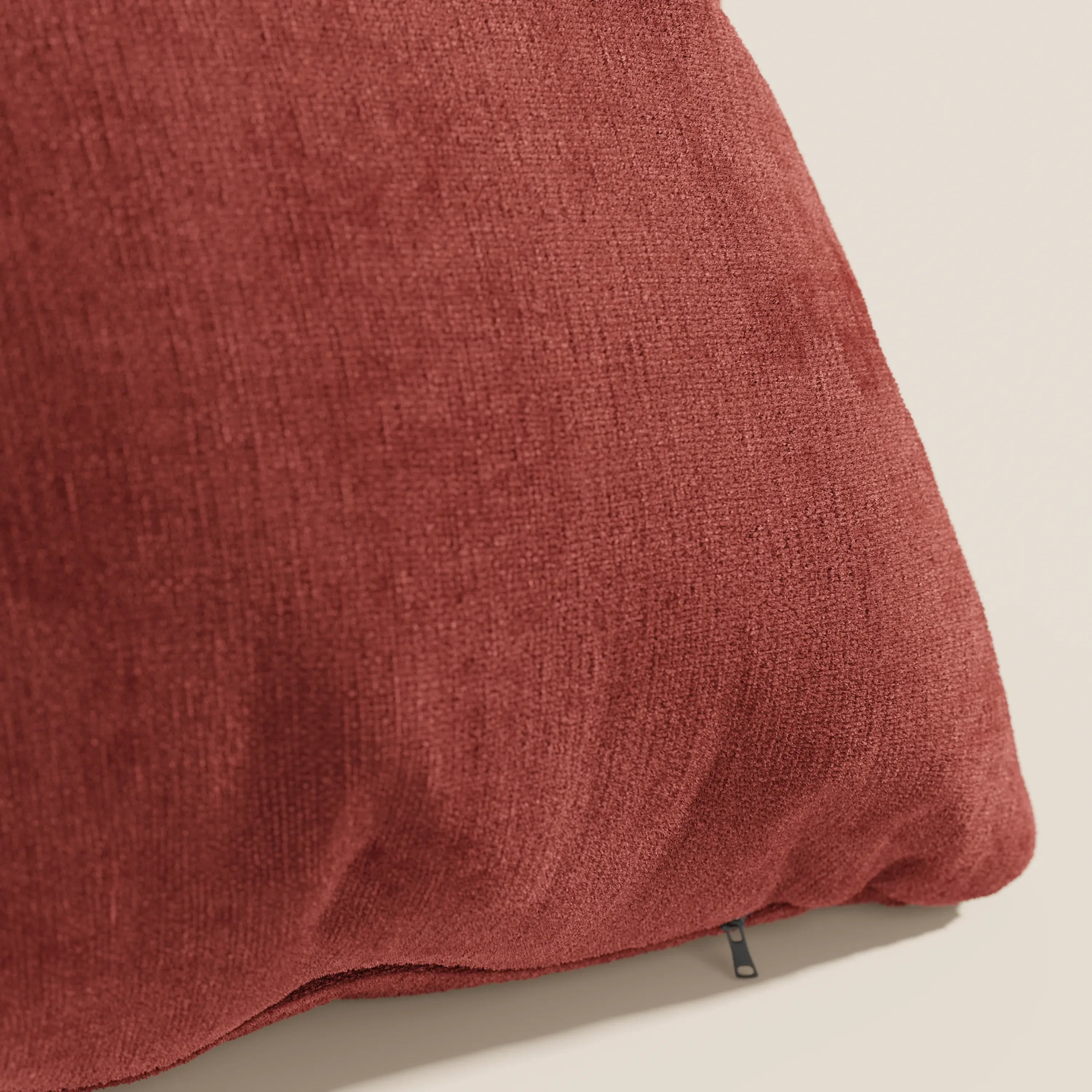 Primo piano del cuscino Bolero rosso ruggine di Divani.Store, realizzato in morbido tessuto T31 antimacchia, impermeabile e non restringente. Il cuscino, leggermente abbondante, è caratterizzato da una piccola cerniera nera su uno sfondo neutro e chiaro.