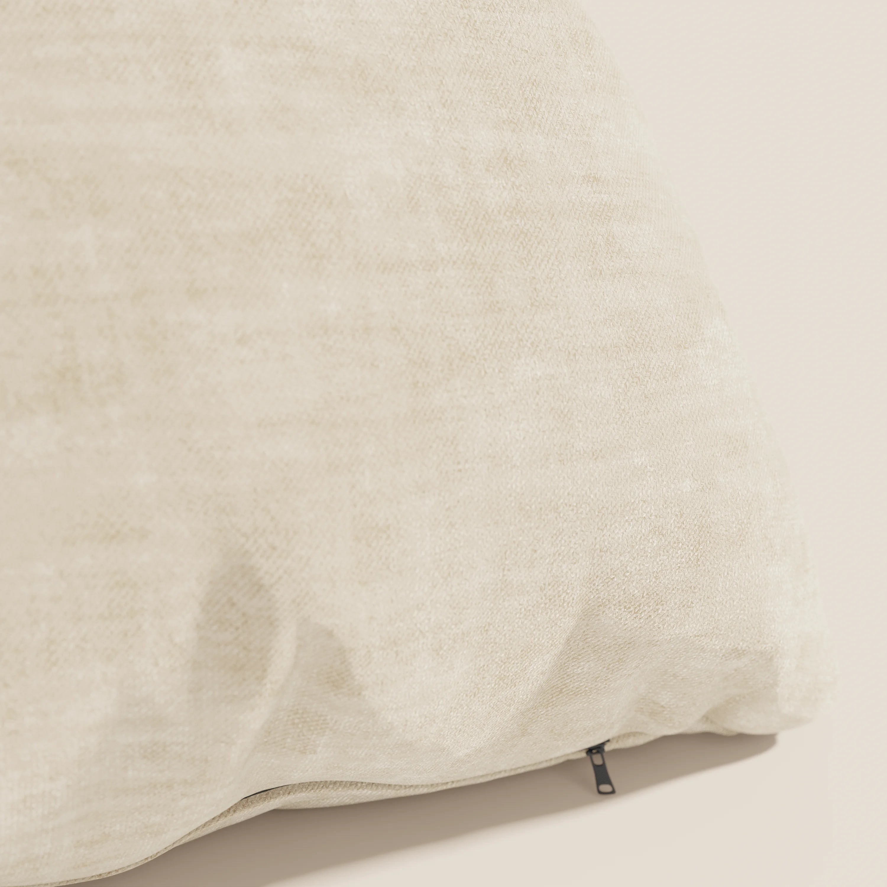 Primo piano del cuscino Sofia di Divani.Store in beige chiaro, caratterizzato da pieghe morbide, una piccola cerniera nera e realizzato in velluto nuvolato Easy Clean T35 smacchiabile e impermeabile per un look neutro e rilassante.