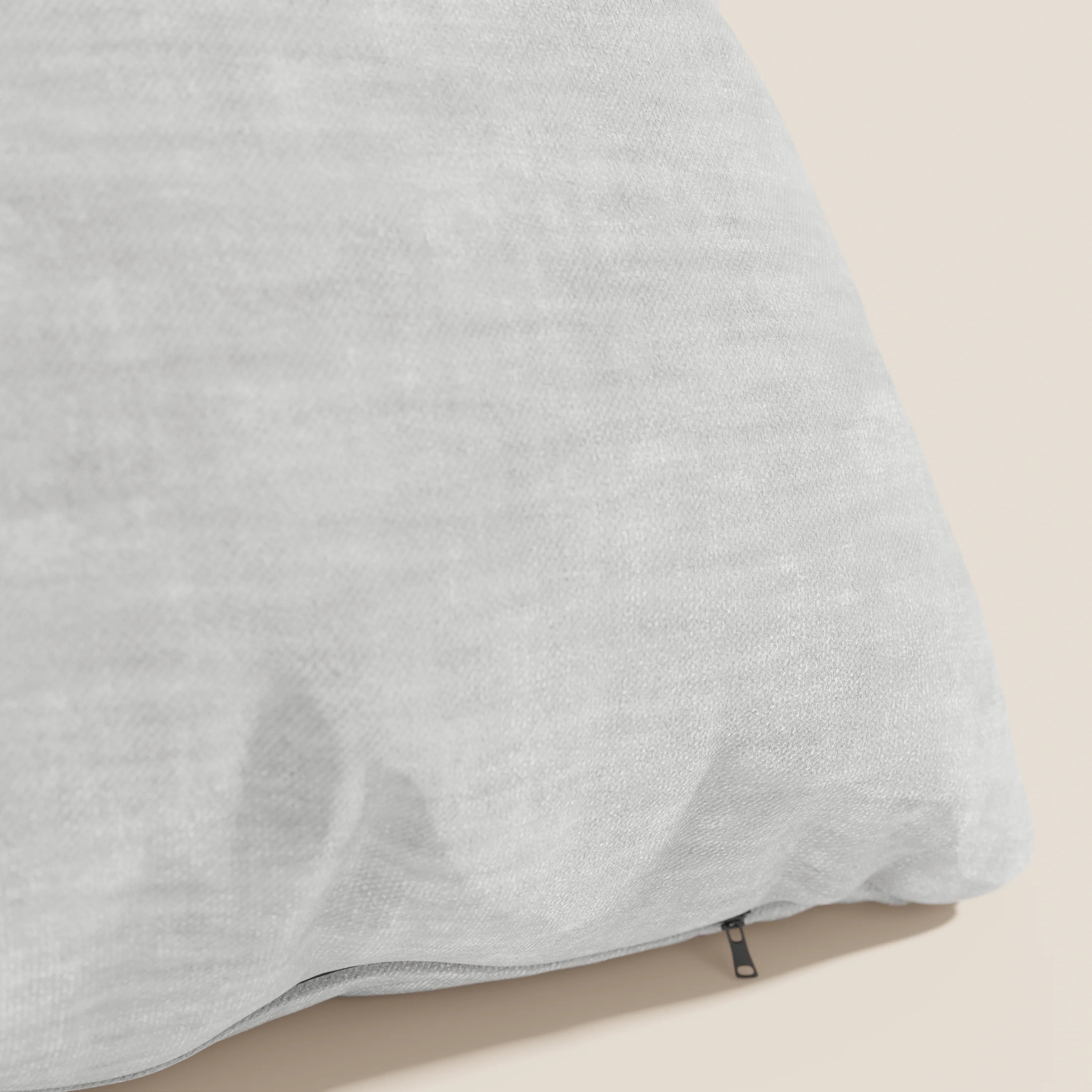Un primo piano di Sofia, il cuscino Divani.Store in morbido velluto nuvolato grigio chiaro, smacchiabile e impermeabile Easy Clean T35, con federa testurizzata e zip nera removibile, su superficie beige. Sfondo semplice e ordinato.