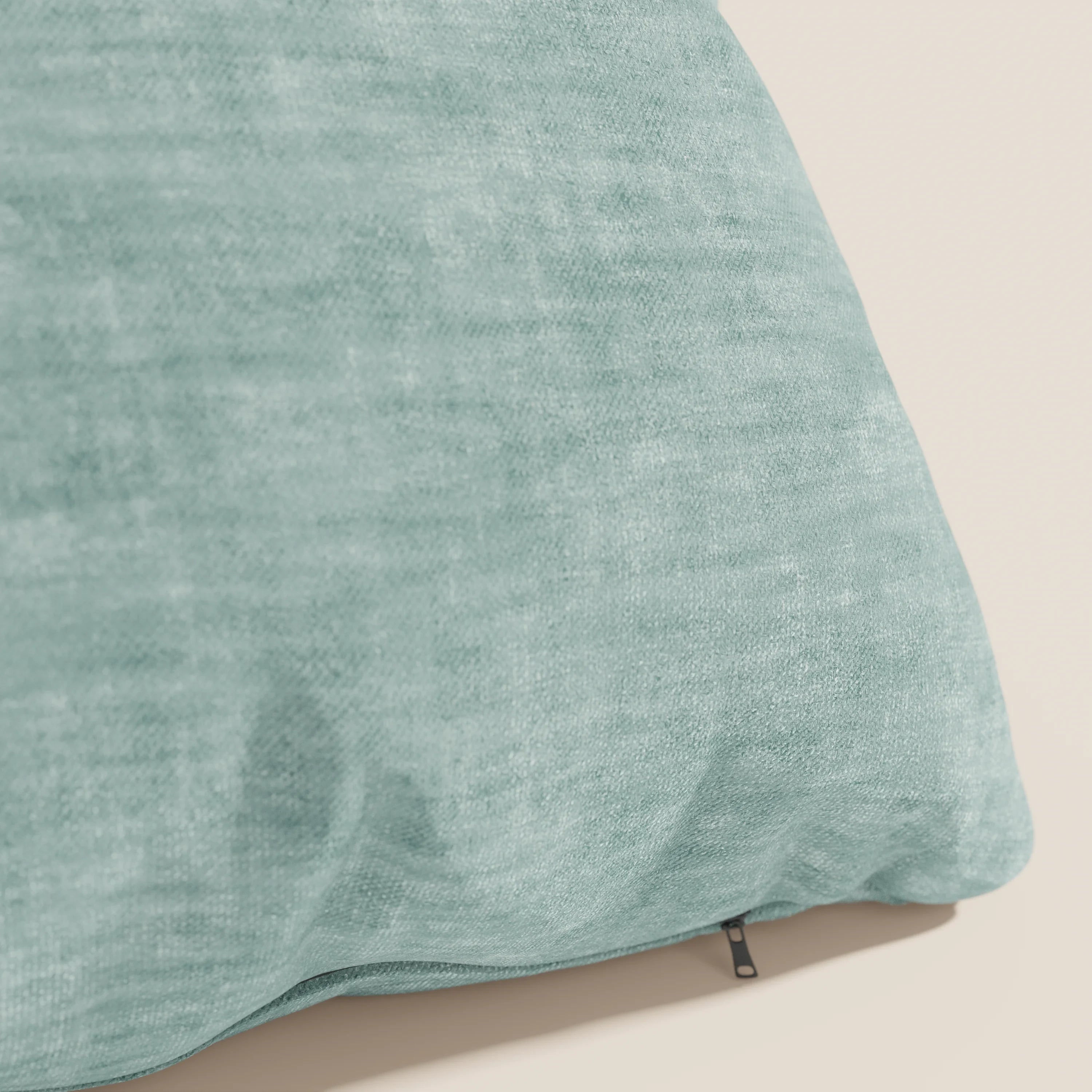 Un primo piano del cuscino Sofia di Divani.Store in verde chiaro mostra il suo morbido tessuto nuvolato velluto Easy Clean T35 con un sottile motivo a chiazze e una piccola cerniera nera, su uno sfondo beige chiaro.
