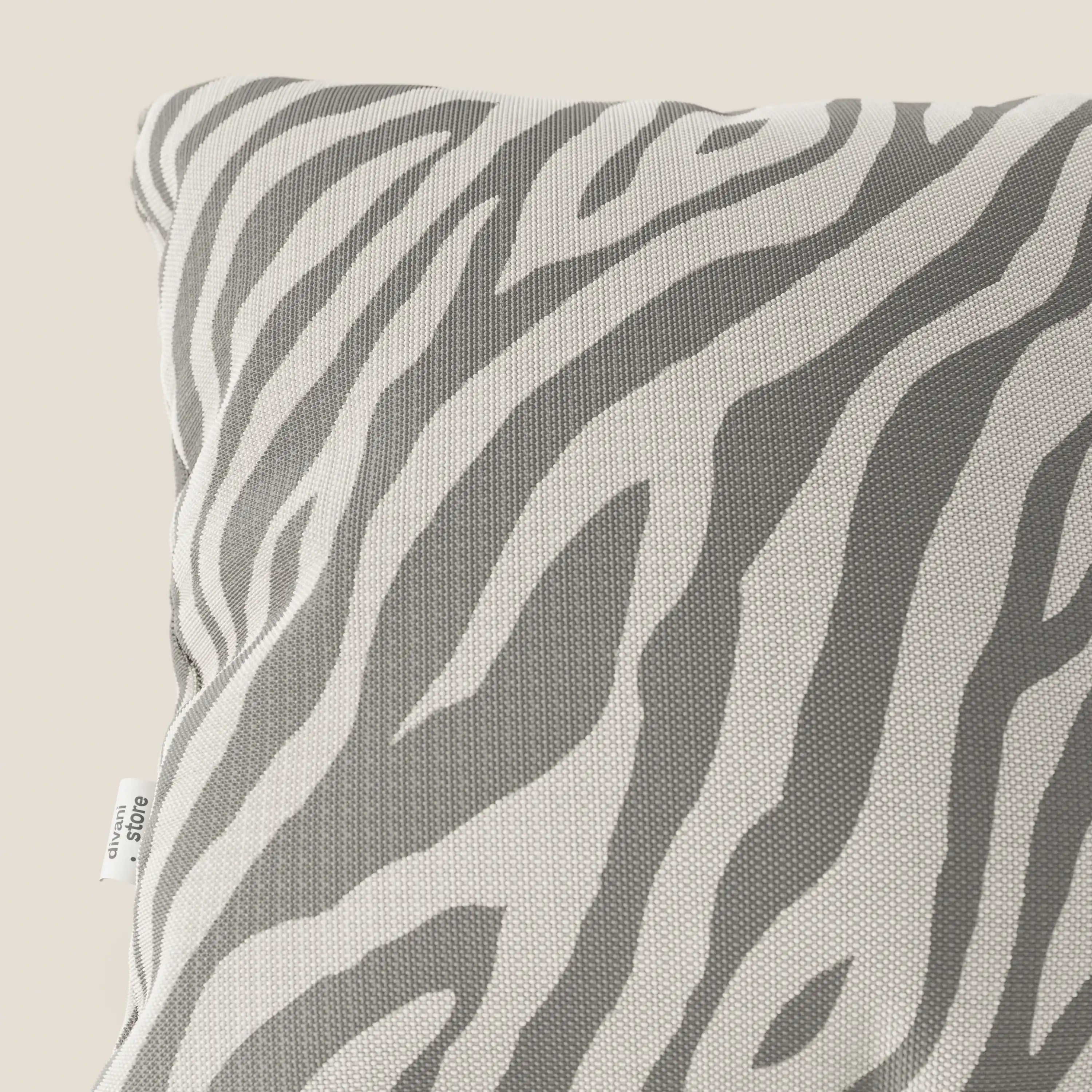 Primo piano del cuscino Divani.Store Stripe geometrici in tessuto Idrorepellente, in grigio e bianco, con una piccola etichetta bianca sulla sinistra. Il cuscino presenta un motivo a strisce geometriche su uno sfondo beige.