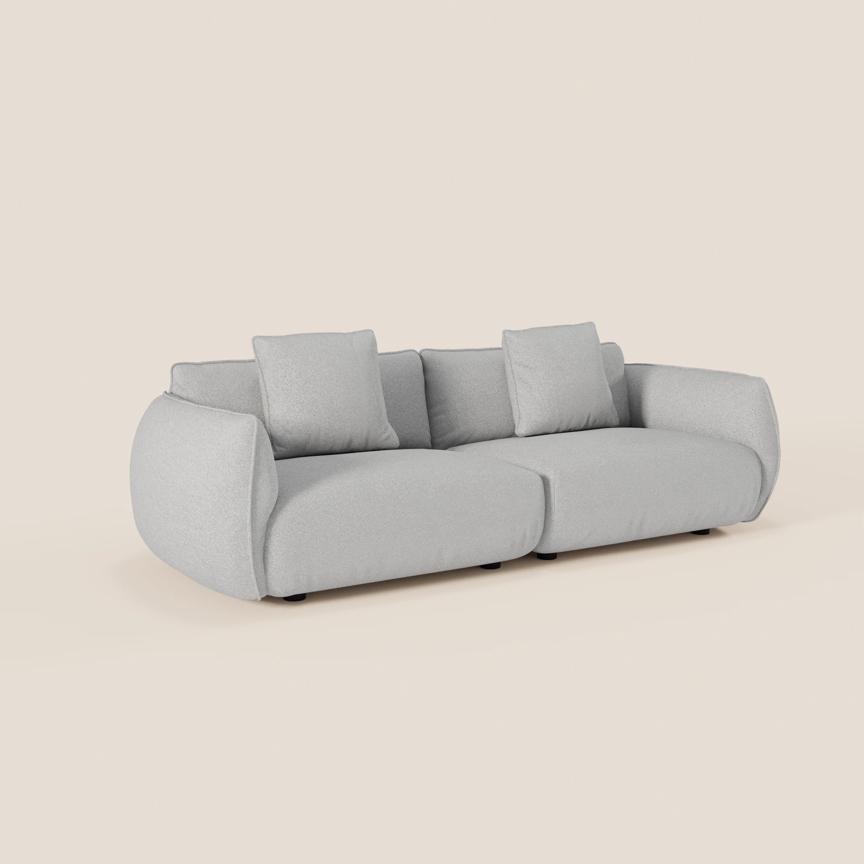Il divano Nimbus 3 posti modulare e componibile di Divani.Store è un moderno divano in tessuto grigio chiaro (250 cm) con bordi arrotondati, cuscini spessi, due ampie sedute e quattro cuscini quadrati coordinati, presentato su uno sfondo bianco sporco.