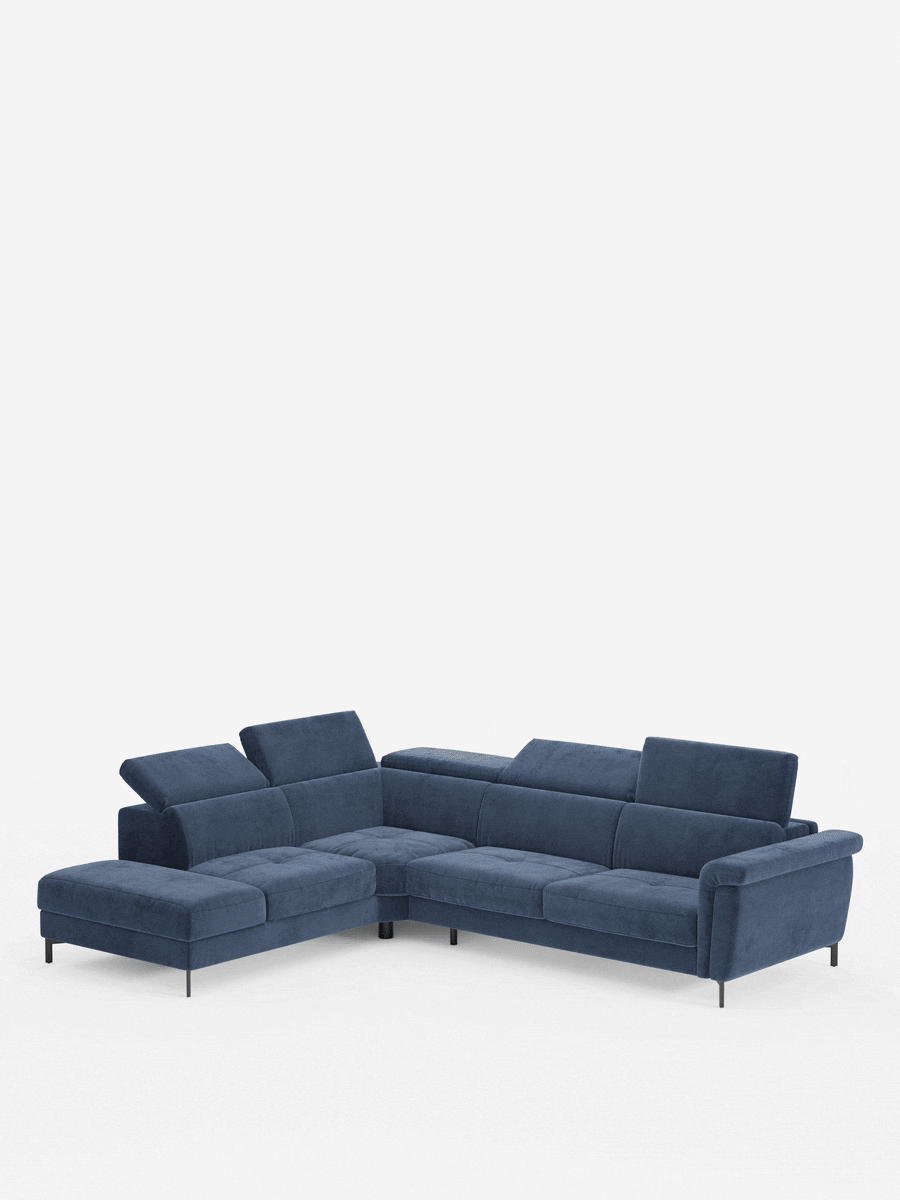 Il divano letto angolare Capri di Divani.Si tratta di un moderno divano componibile a forma di L rivestito in vellutino smacchiabile blu scuro, dotato di tre ampie sedute, una chaise longue integrata, poggiatesta regolabili, un materasso ad alte prestazioni (T30) e sottili gambe nere, raffigurato su uno sfondo bianco a tinta unita.