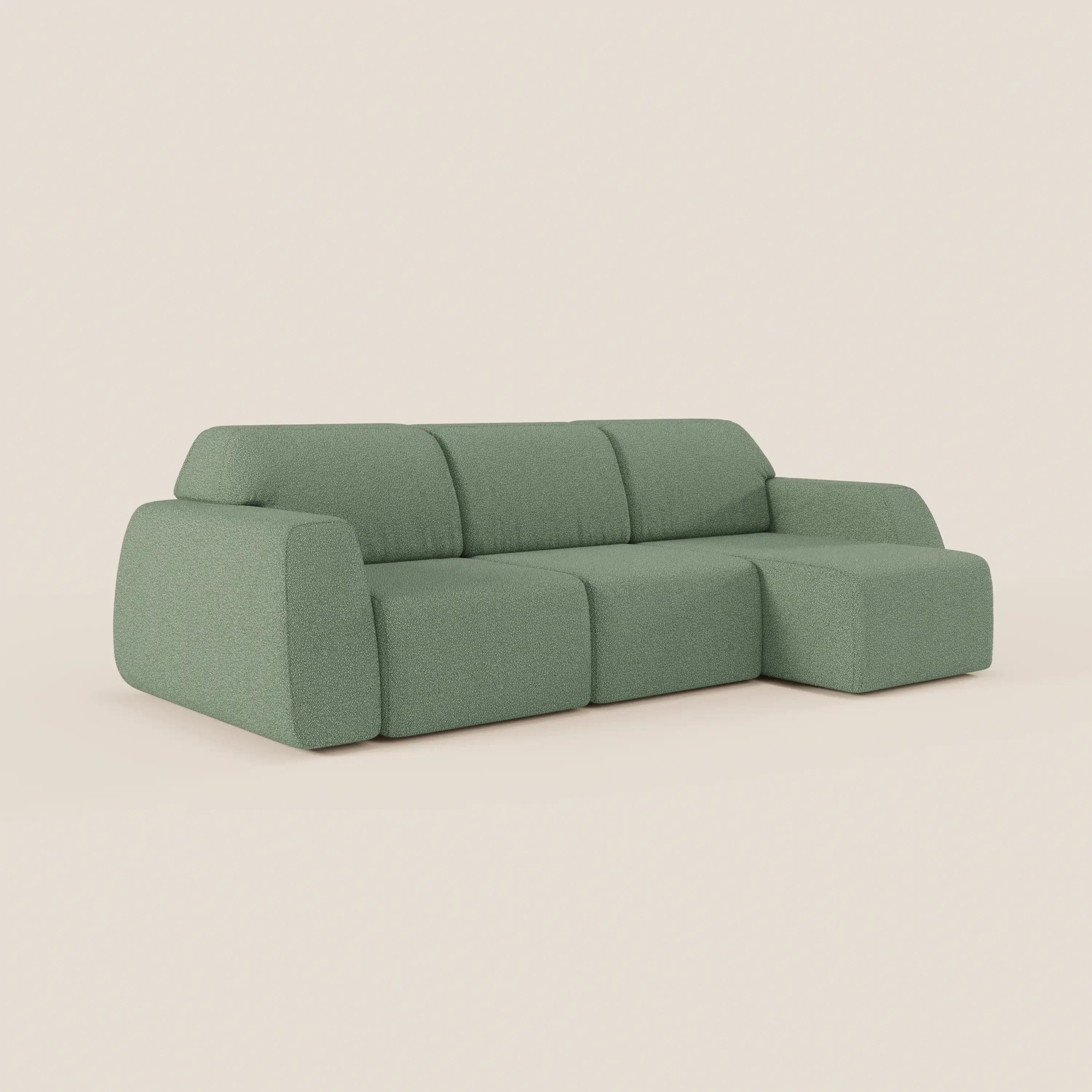 Il divano angolare Orbit con penisola reversibile di Divani.Store, in tessuto smacchiabile effetto cotone T33 verde salvia, presenta sedute allungabili, cuscini morbidi e design moderno dai bordi arrotondati su sfondo beige neutro.