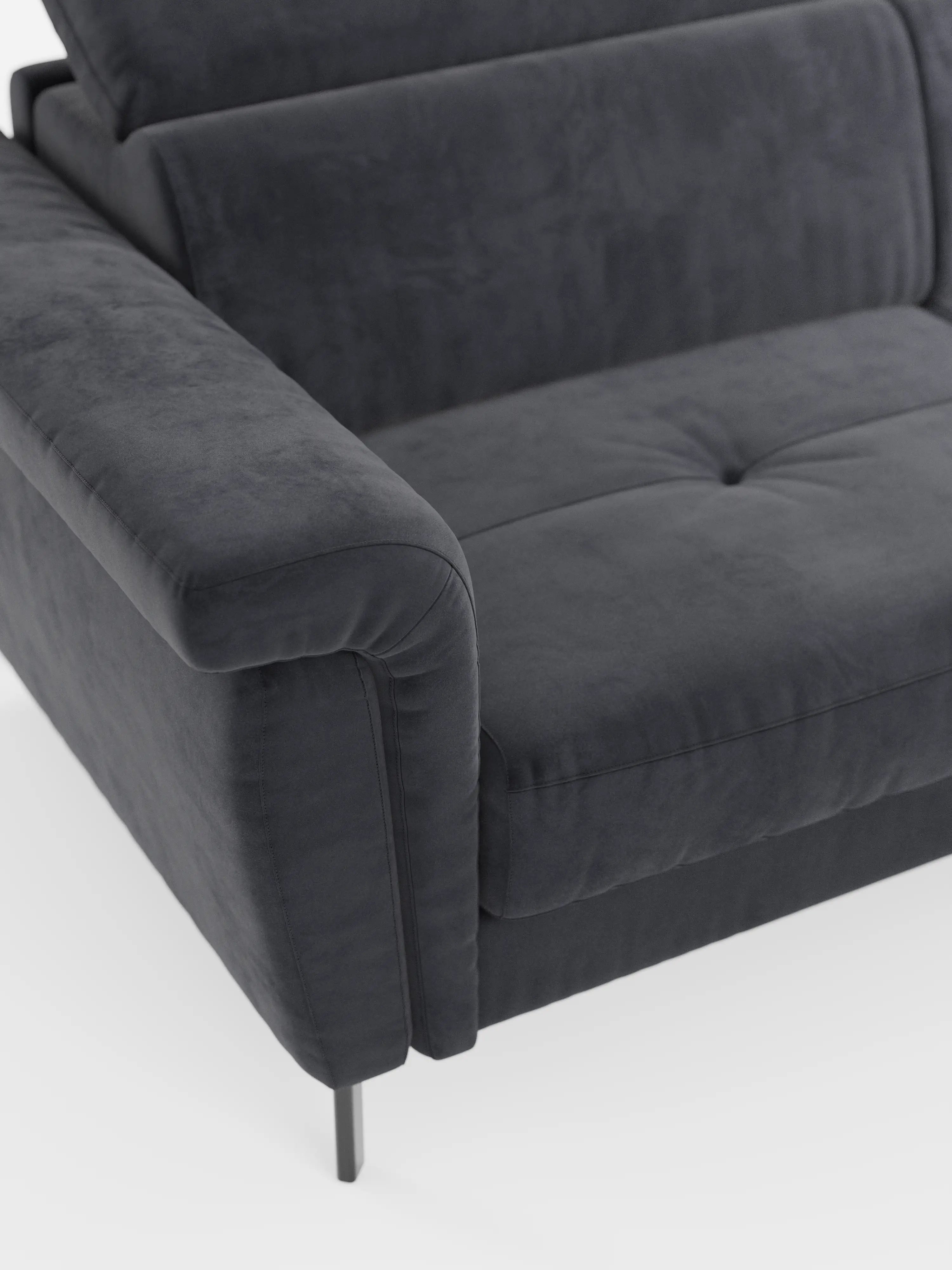 Primo piano del divano letto di design Capri con piedini alti di Divani.Store, che mette in risalto il bracciolo sinistro, il morbido cuscino di seduta con delicati dettagli trapuntati e l'elegante gamba in metallo. Rivestito in raffinato tessuto effetto velluto smacchiabile T30 dall’aspetto particolarmente morbido e lussuoso, questo moderno divano grigio scuro presenta una superficie vellutata. Lo sfondo è bianco a tinta unita.