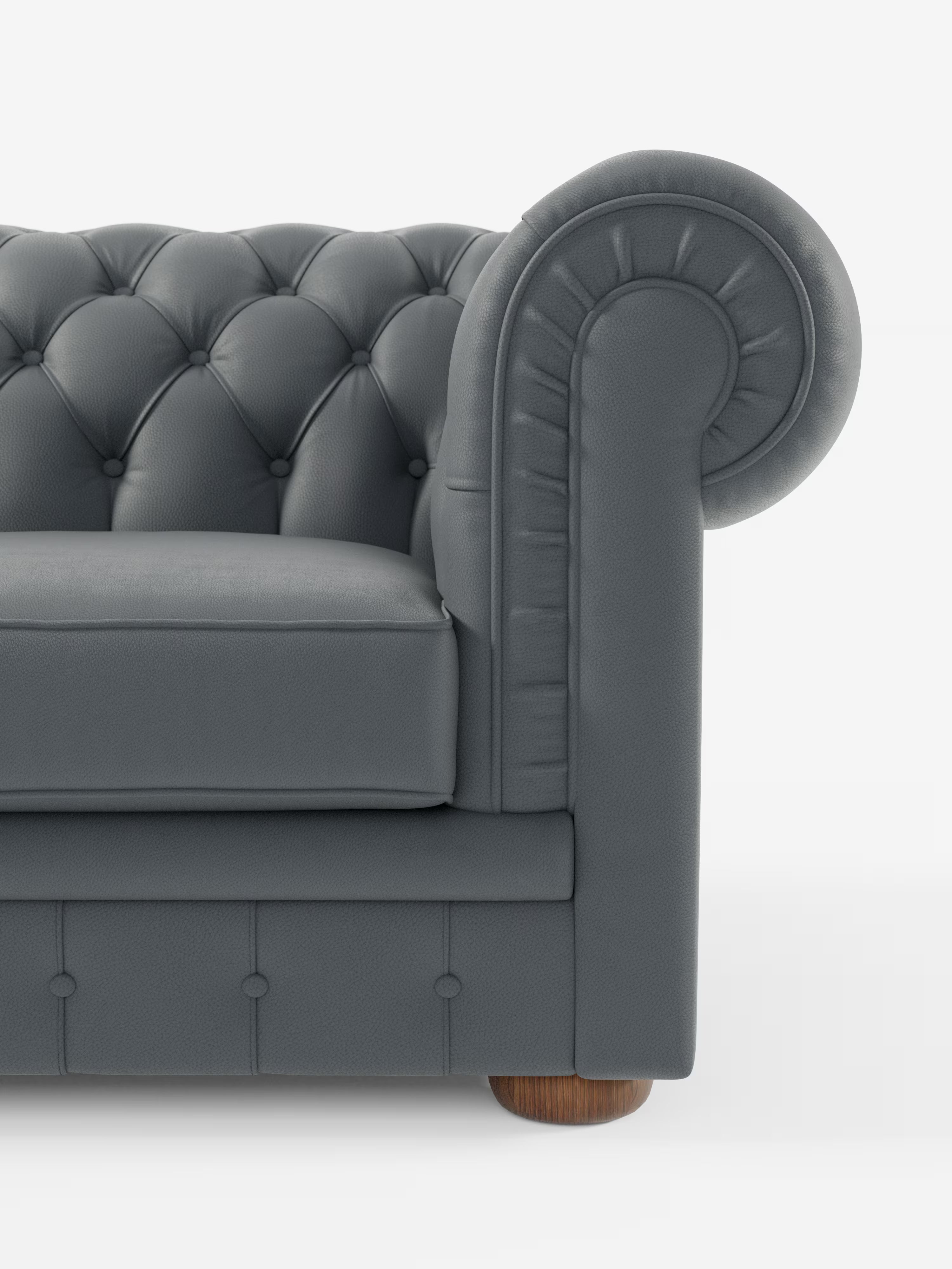 Un primo piano del divano Chester 4 Posti 3 sedute in Vera Pelle – Chesterfield Capitonné Artigianale di Divani.Store, che ne mette in risalto il rivestimento in vera pelle capitonné grigio scuro, i braccioli arrotondati, i dettagli a bottoni e una parte del cuscino di seduta. Il divano, realizzato artigianalmente, presenta gambe in legno ed è posizionato su uno sfondo bianco a tinta unita.