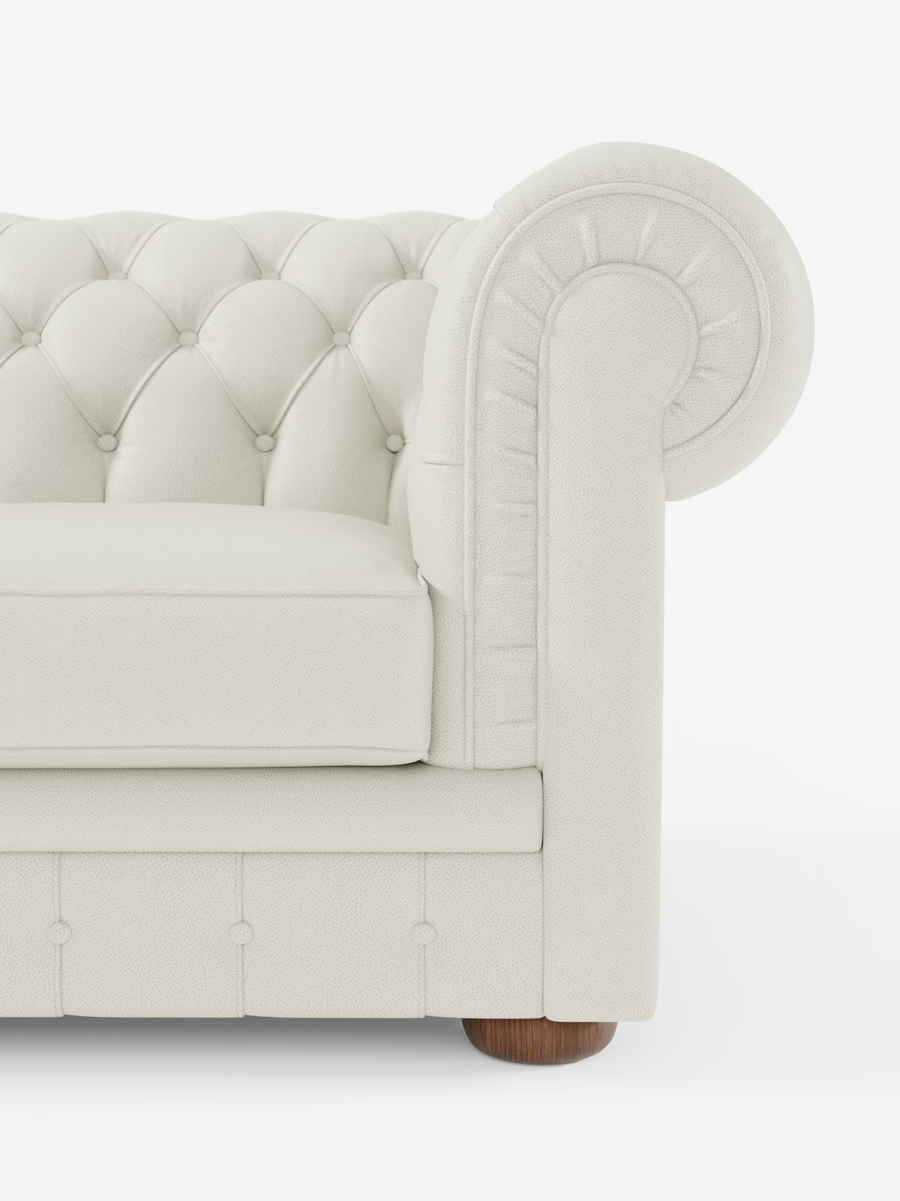 Primo piano di un divano Chester 4 Posti 3 sedute in vera pelle, color crema, con braccioli in stile Chesterfield capitonné artigianale, caratterizzato dai tipici bottoni decorativi, braccioli arrotondati, morbido cuscino di seduta e gambe rotonde in legno. Realizzato a mano con maestria in Italia da Divani.Store in vera pelle, il divano si distingue per la ricca trama e il design lussuoso che risaltano sullo sfondo bianco. Nell’immagine è raffigurata solo una parte del divano.
