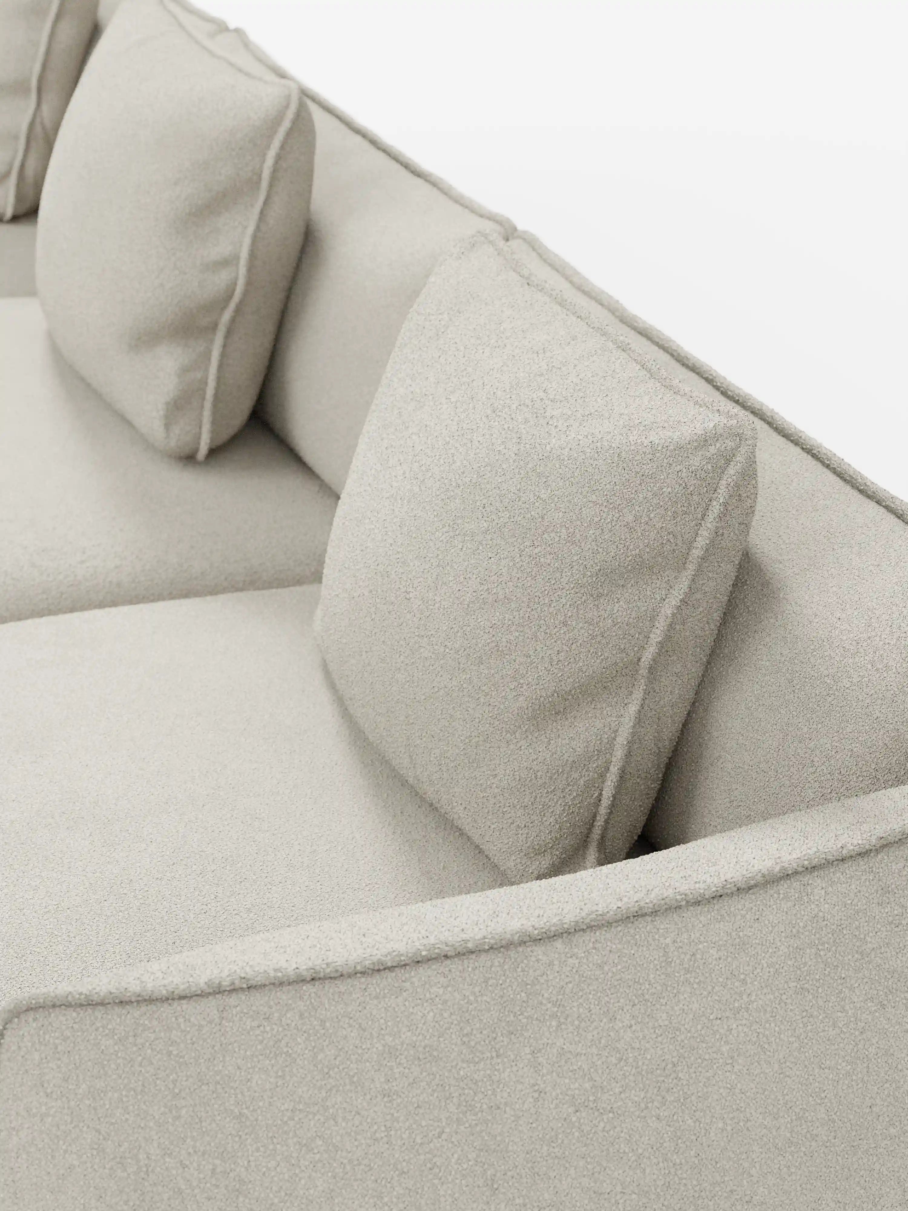Primo piano del divano modulare a 3 posti “Nimbus” di Divani.Store, rivestito in morbido tessuto T33 effetto cotone, resistente alle macchie, color beige chiaro. Questo divano moderno è caratterizzato da due morbidi cuscini quadrati dello schienale, braccioli imbottiti, linee pulite e un design minimalista. Lo sfondo è bianco a tinta unita.