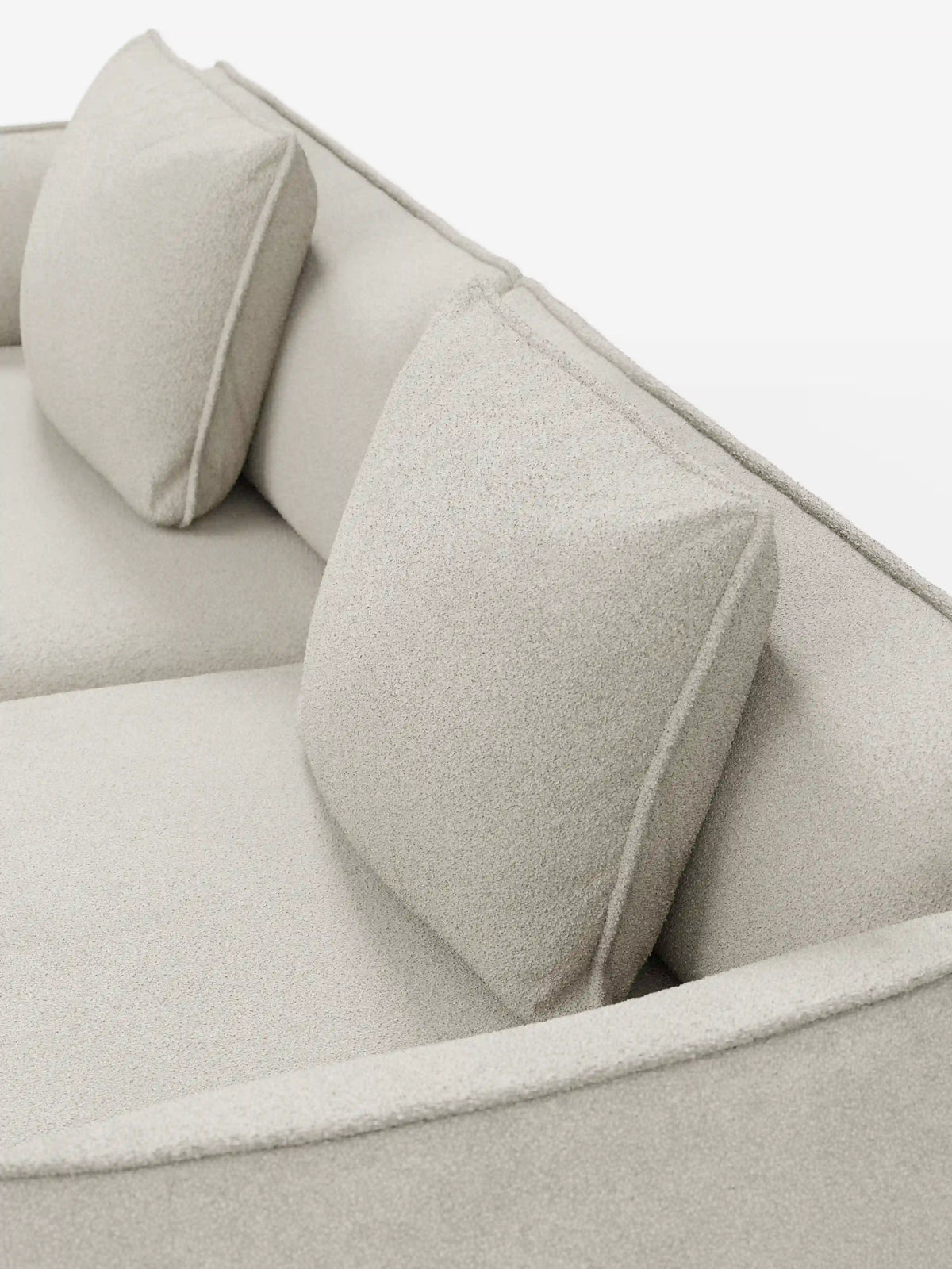 Un primo piano del divano modulare e componibile a 3 posti Nimbus da 250 cm di Divani.Store, un elegante divano modulare beige chiaro rivestito in tessuto smacchiabile effetto cotone T33. Questo modello sfoderabile presenta due cuscini quadrati coordinati per lo schienale, linee pulite e minimaliste e una seduta morbida con rivestimento testurizzato che unisce eleganza e praticità, il tutto su uno sfondo bianco.