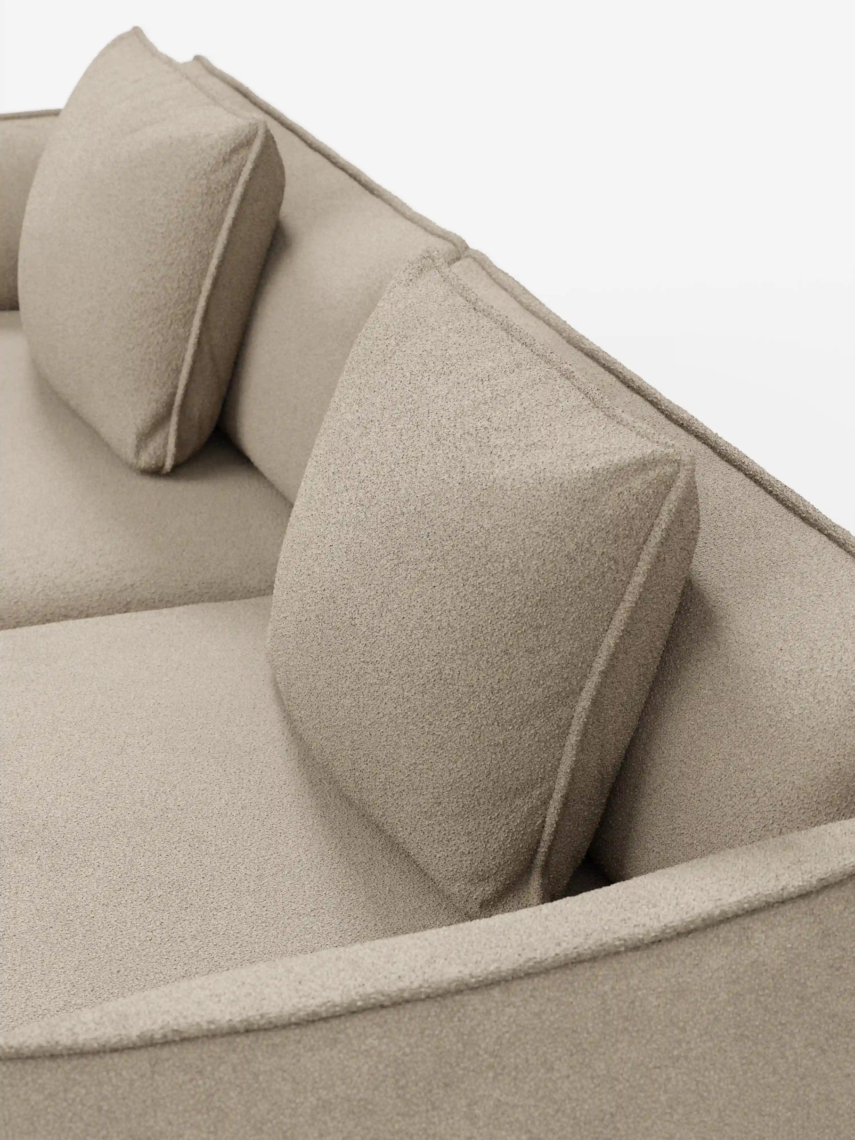 Primo piano del divano Nimbus a 3 posti, modulare e componibile da 250 cm di Divani.Store, rivestito in tessuto effetto cotone beige (t33), sfoderabile e antimacchia. Il divano modulare presenta due cuscini schienali quadrati e una seduta liscia dall’aspetto morbido e strutturato. La foto è stata scattata da una prospettiva obliqua dall’alto su uno sfondo bianco a tinta unita.