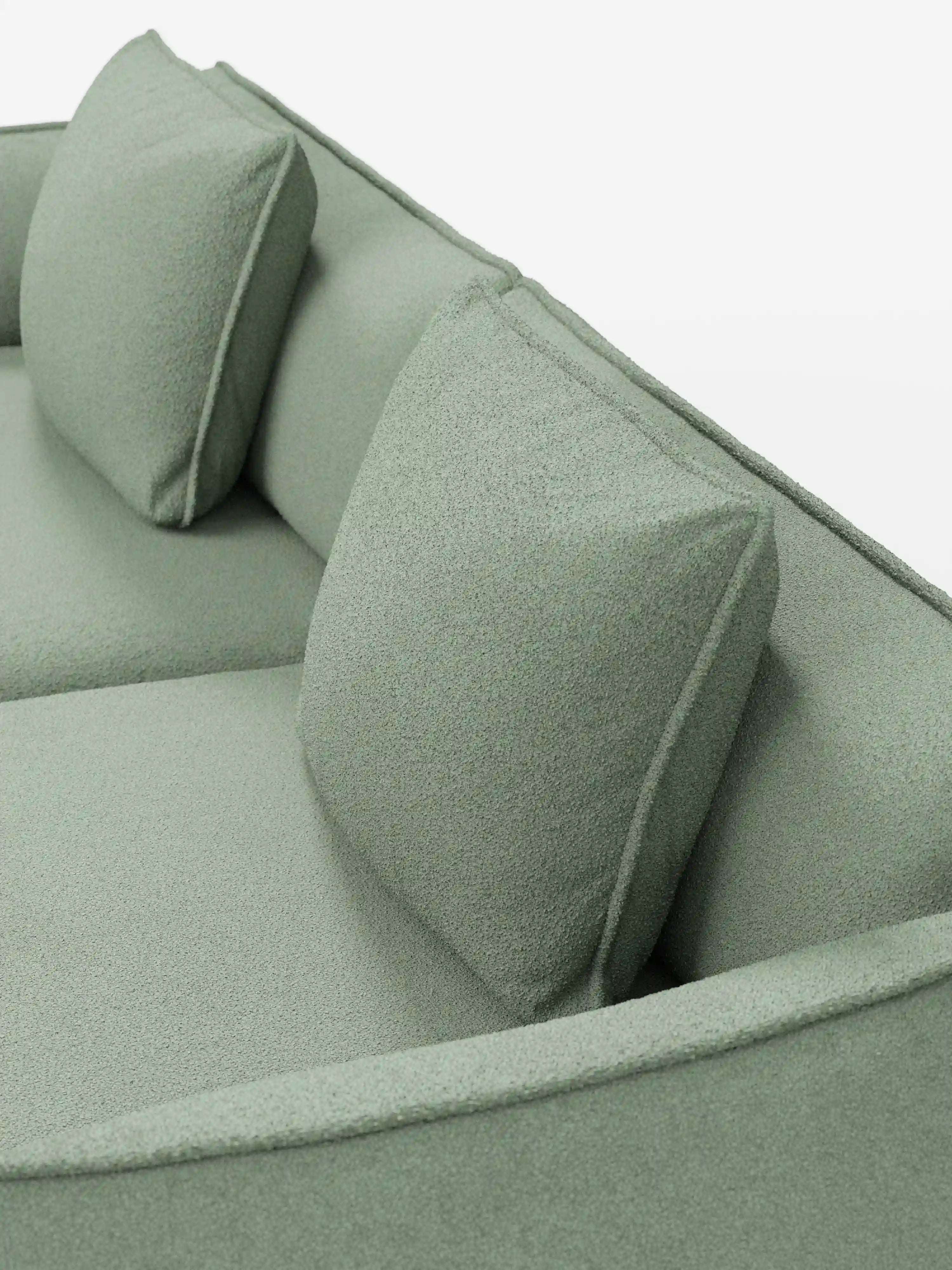Un primo piano del divano a 3 posti modulare e componibile Nimbus di Divani.Store, lungo 250 cm e rivestito in tessuto T33 effetto cotone di colore verde chiaro, resistente alle macchie. Il divano presenta due grandi cuscini dello schienale di forma squadrata dall’aspetto testurizzato, il tutto disposti con cura su uno sfondo bianco a tinta unita.
