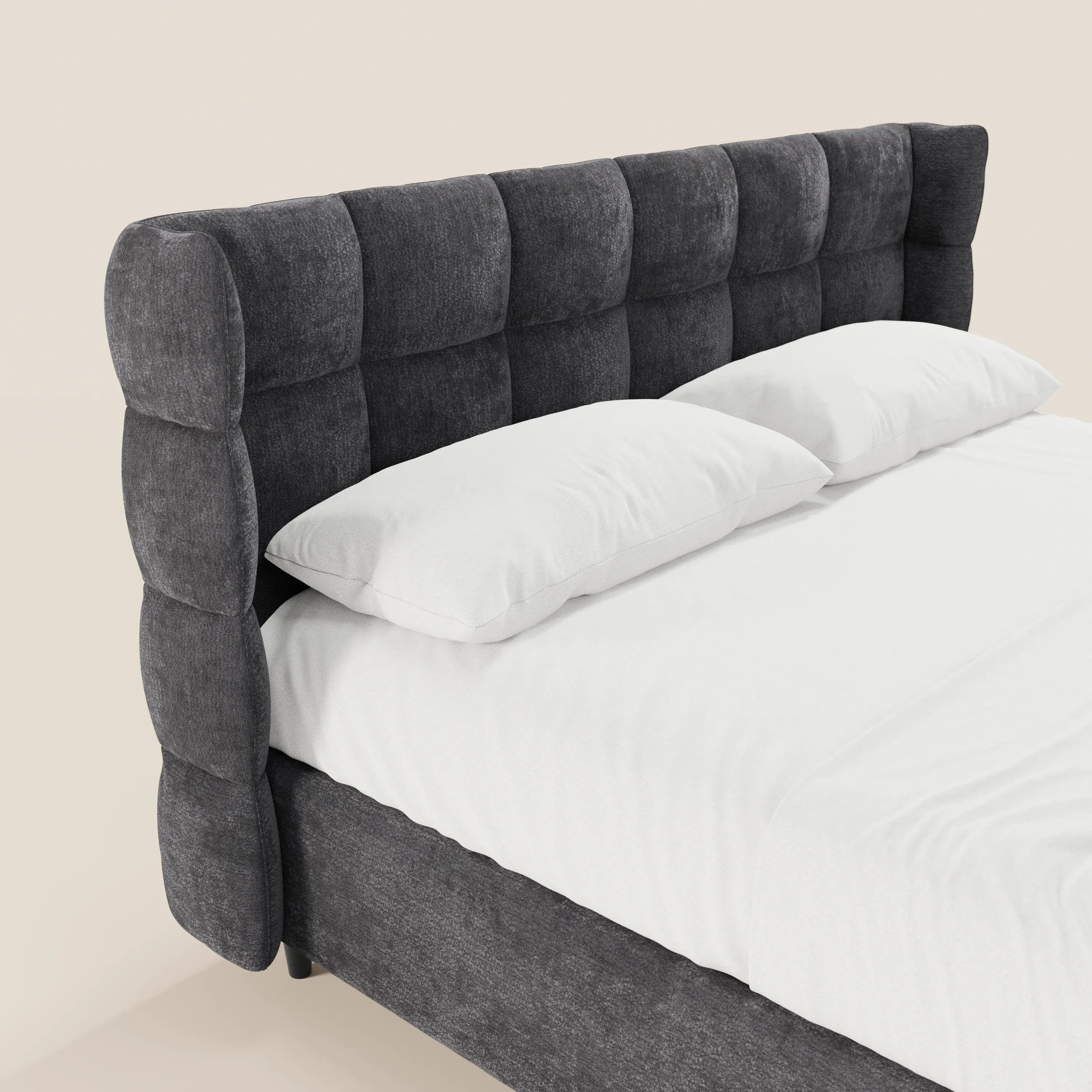Il letto imbottito RAGNAR di Letti.store è rivestito in tessuto grigio scuro certificato Oeko-Tex® e presenta una testiera avvolgente capitonné con imbottitura a quadri. Con le lenzuola bianche e i due cuscini disposti con cura, risalta su uno sfondo chiaro.