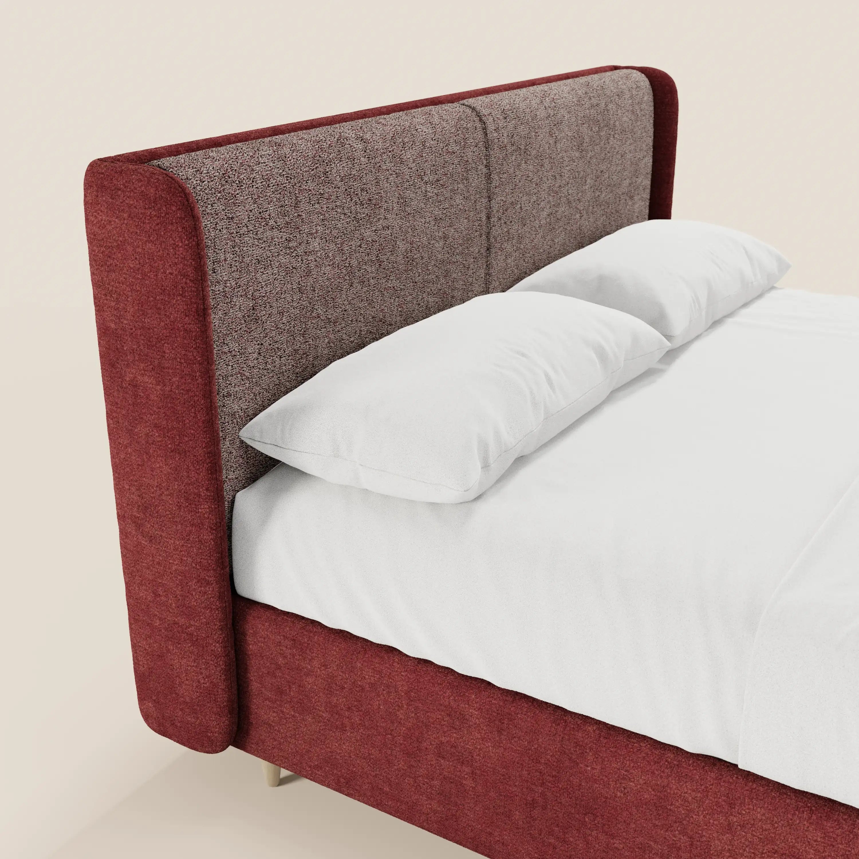 Il letto imbottito bicolore VALKIRIA di Letti.store presenta una struttura rivestita di un rosso intenso e una testiera curva marrone chiaro con finitura ruvida, rifinita con cura con biancheria da letto bianca. Su uno sfondo a tinta unita è visibile solo un angolo.