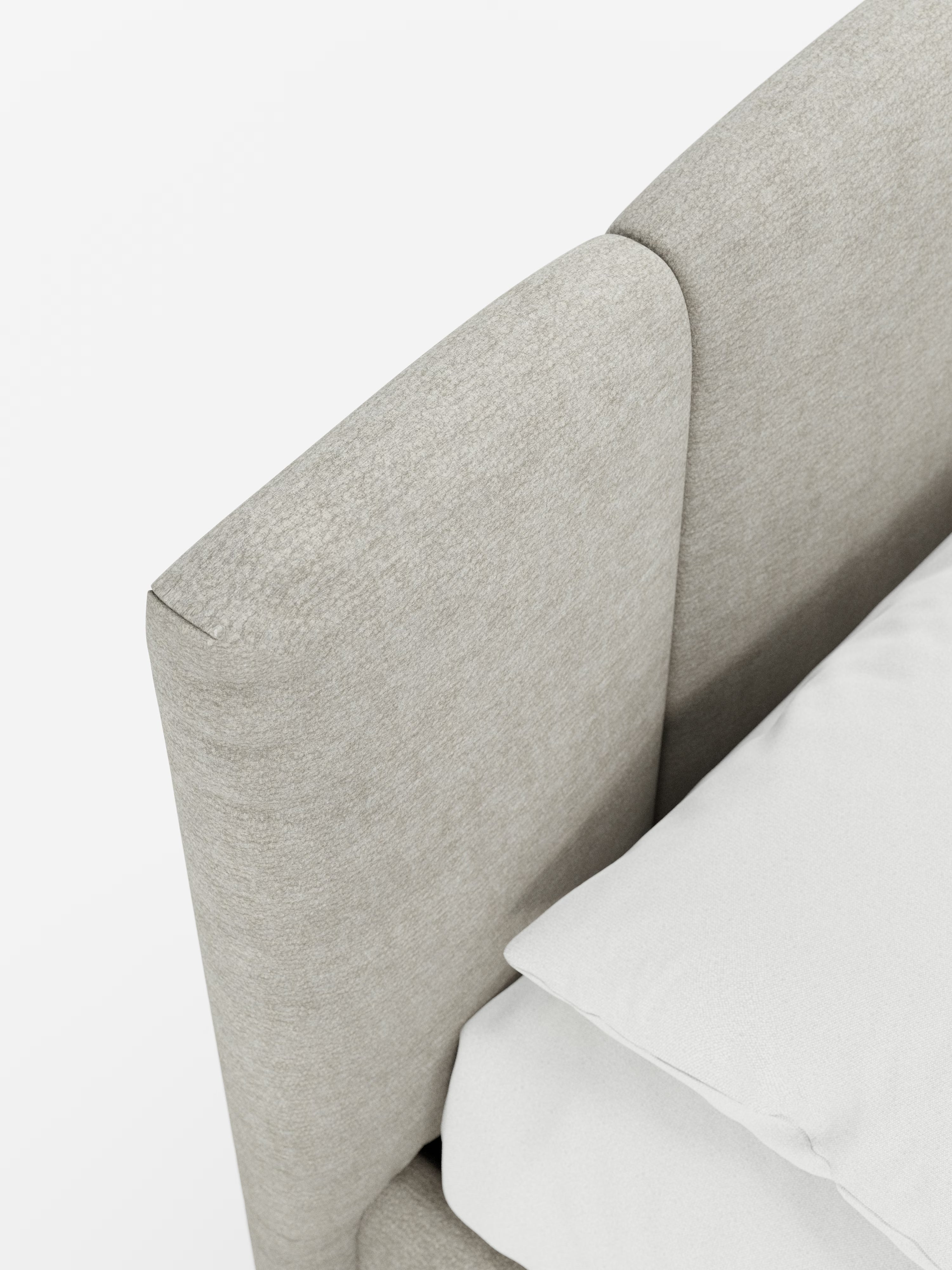 Primo piano del letto imbottito ARKAM con contenitore e testiera a lavorazione verticale di Letti.store, caratterizzato da una moderna testiera imbottita in tessuto grigio chiaro certificato Oeko-Tex® con morbidi angoli arrotondati. Un cuscino e un lenzuolo di un bianco candido riposano sul materasso, creando un look pulito, minimalista e accogliente su uno sfondo bianco a tinta unita: un elegante esempio di design shabby chic per un letto moderno.