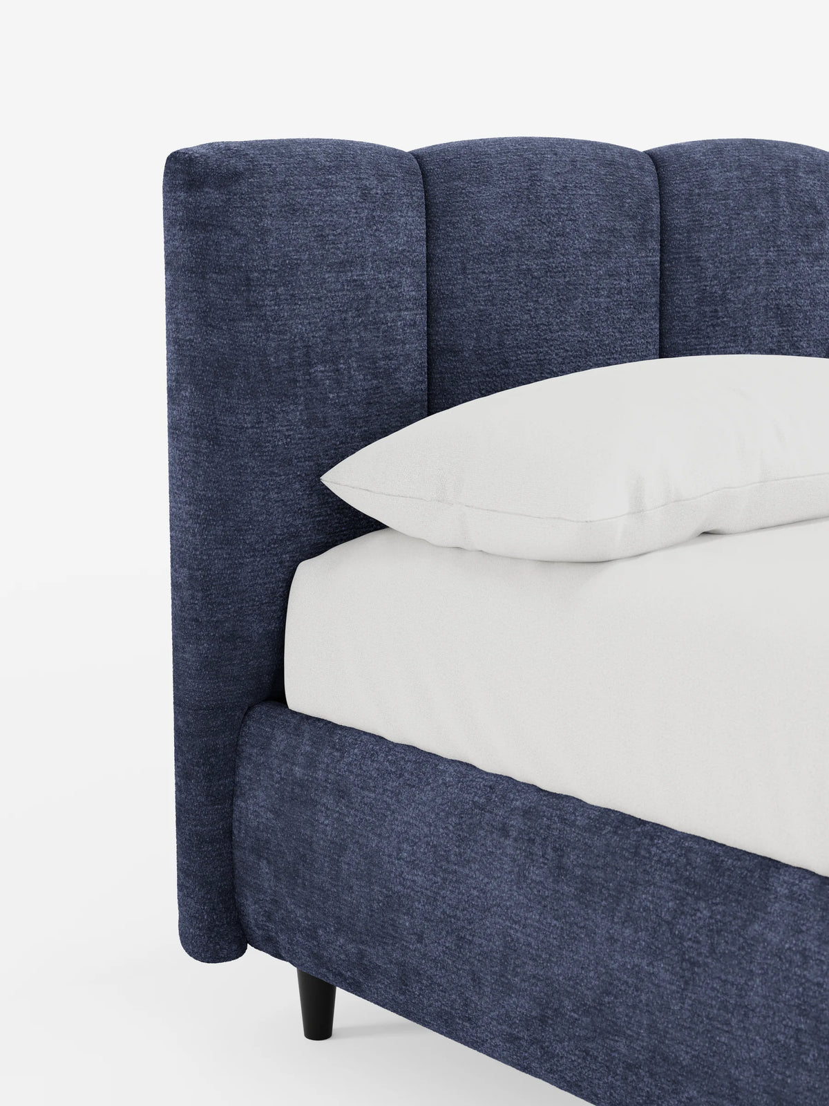 Un primo piano di un letto imbottito ARKAM blu navy con contenitore e testiera a pannellatura verticale, caratterizzato da una testiera alta a pannellatura verticale, dalla morbida trama del tessuto, dalla biancheria da letto bianca e da un unico cuscino su uno sfondo chiaro e semplice.