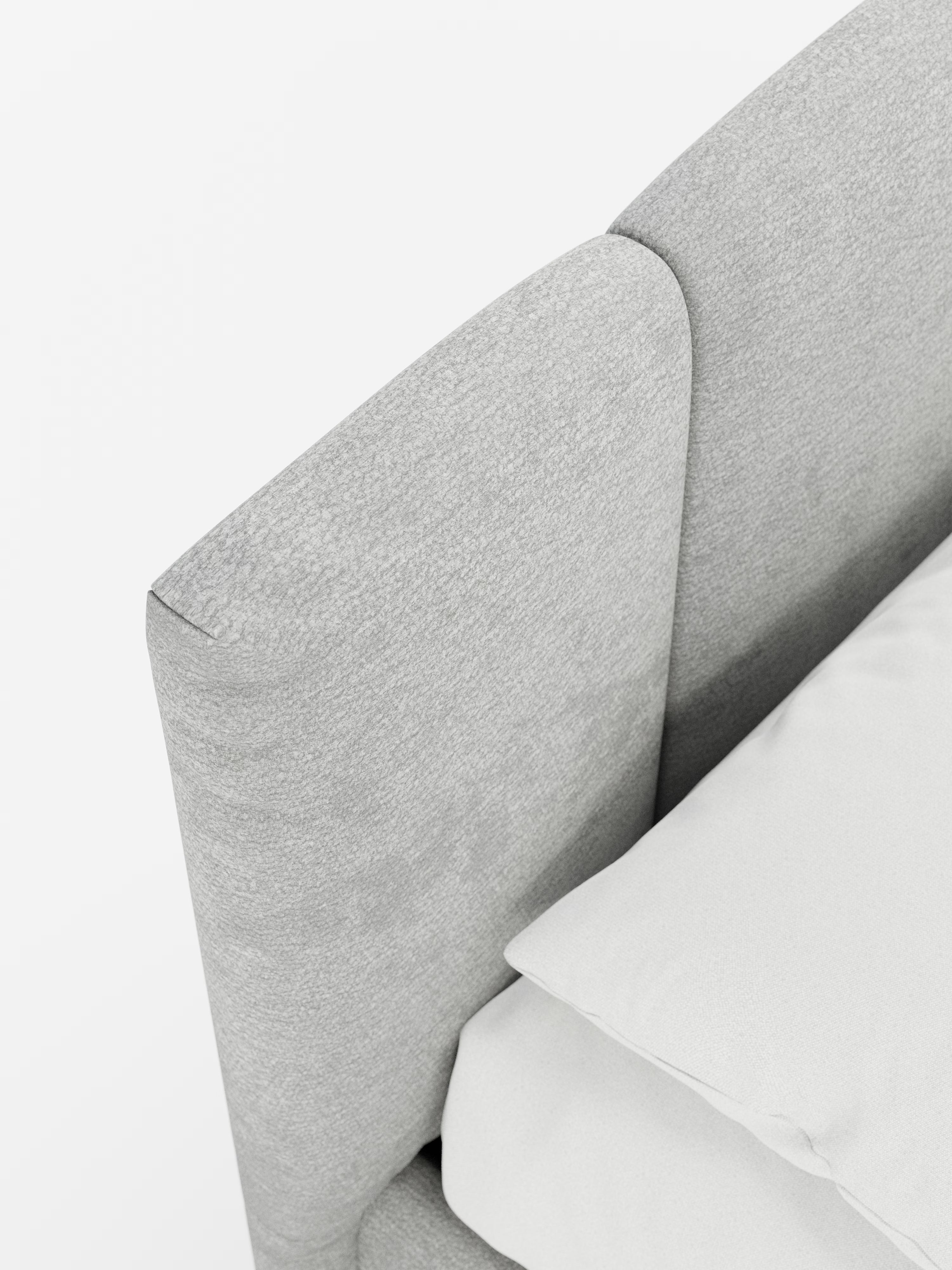 Primo piano del letto imbottito ARKAM di Letti.store, caratterizzato da una testiera grigio chiaro con cuciture verticali in tessuto certificato Oeko-Tex® e dal raffinato design curvo. La testiera fa da cornice a un cuscino bianco e a un lenzuolo disposti con cura, mettendo in risalto la morbida consistenza e lo stile shabby chic pulito e minimalista sullo sfondo bianco.