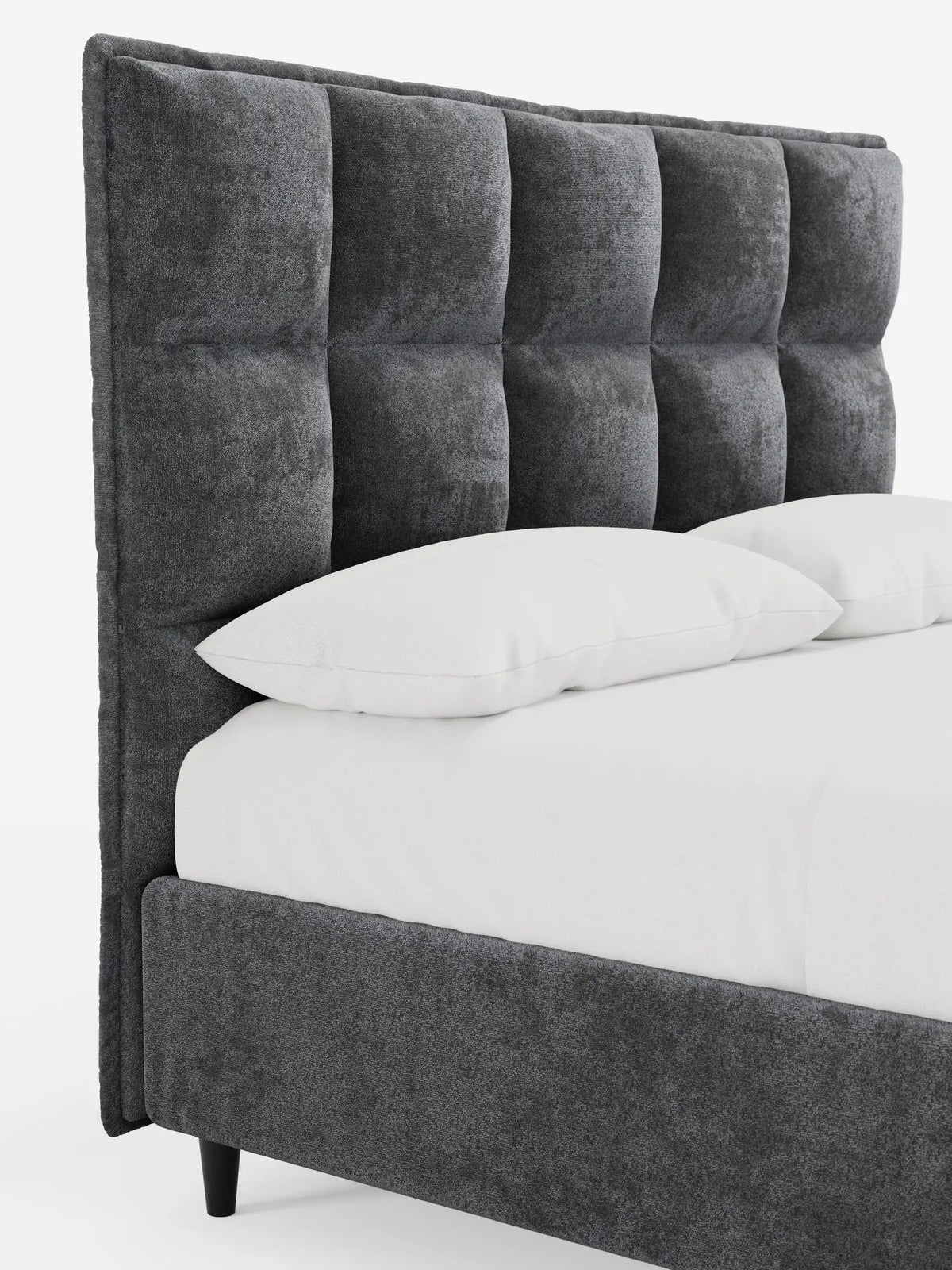 Un letto imbottito AURO grigio scuro con contenitore e testiera alta capitonné in ciniglia Oeko-Tex®, caratterizzato da una testiera alta a griglia capitonné, con due cuscini bianchi e biancheria da letto bianca che risaltano sul tessuto dalla trama ruvida e morbida al tatto.