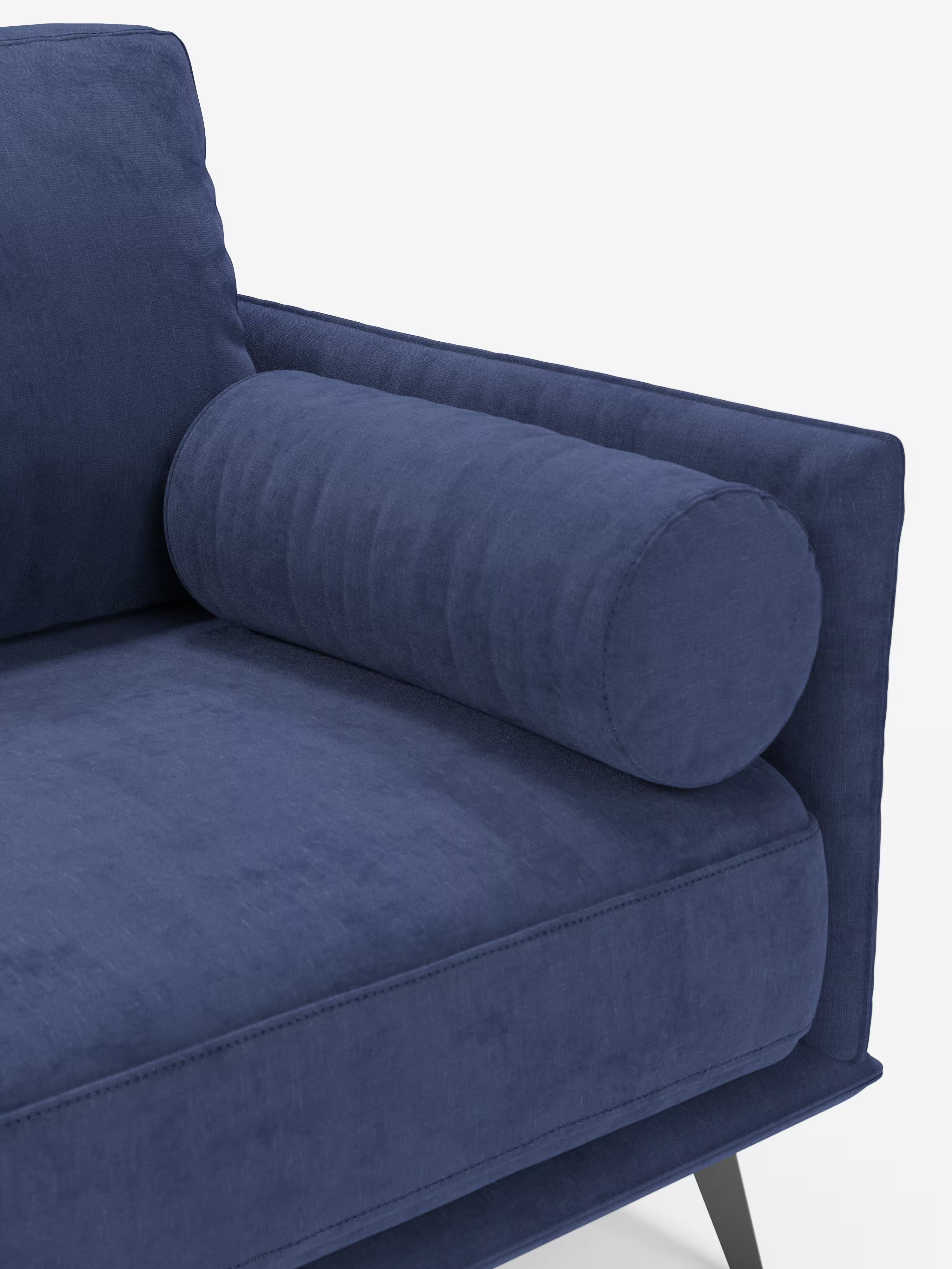 Un primo piano del Basalto Divano lineare a 2 o 3 posti con seduta unica e base in metallo, rivestito in tessuto smacchiabile T31 di Divani.Store, in un ricco tessuto blu navy. Il divano presenta un cuscino cilindrico sul bracciolo, con cuscini morbidi e lisci e braccioli realizzati in tessuto resistente e antimacchia per garantire una qualità duratura. Linee pulite e un design minimalista ne definiscono il fascino moderno, mentre alla base è visibile parte della gamba angolata in metallo nero.