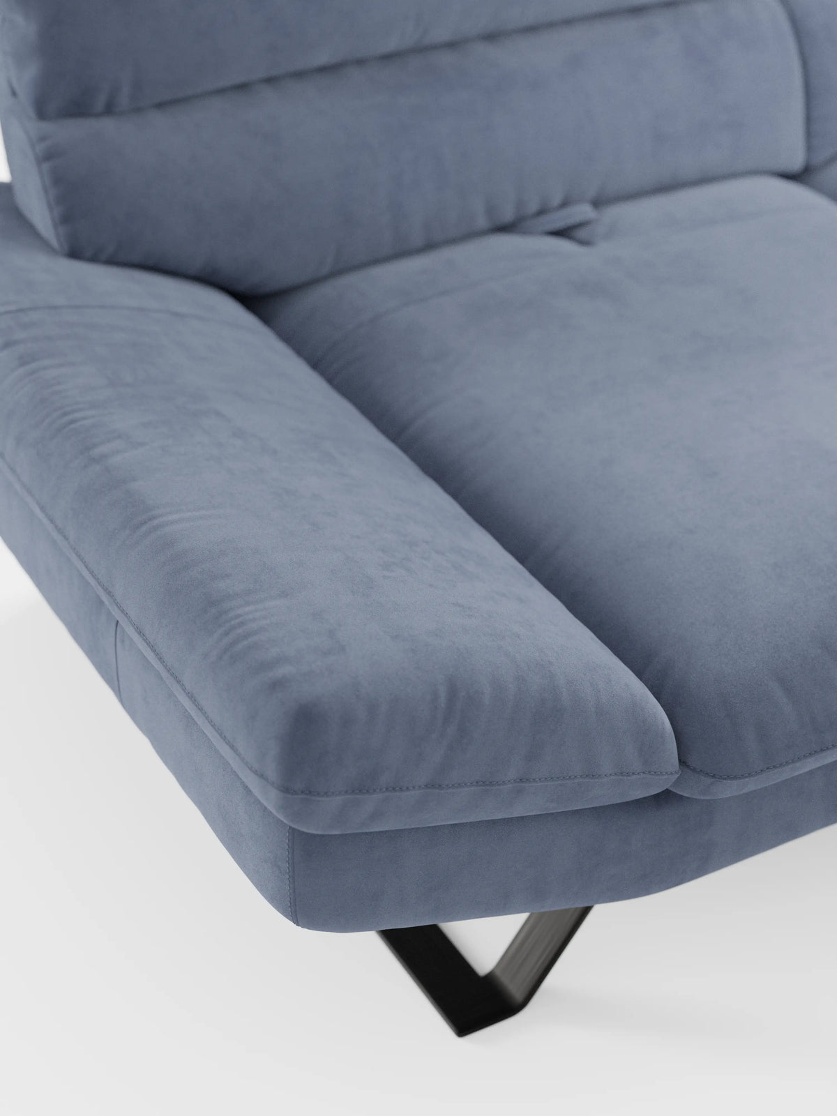 Primo piano del divano Eclipse, dal design moderno, a 2 e 3 posti con schienali traslanti, di Divani.Store, rivestito in morbida microfibra T11 smacchiabile di colore azzurro chiaro. Si notano chiaramente l’ampio bracciolo e il cuscino di seduta, con eleganti gambe alte in metallo nero che spuntano parzialmente da sotto. Dotato di seduta modulabile per un maggiore comfort e flessibilità, la superficie liscia e morbida risalta sullo sfondo bianco.