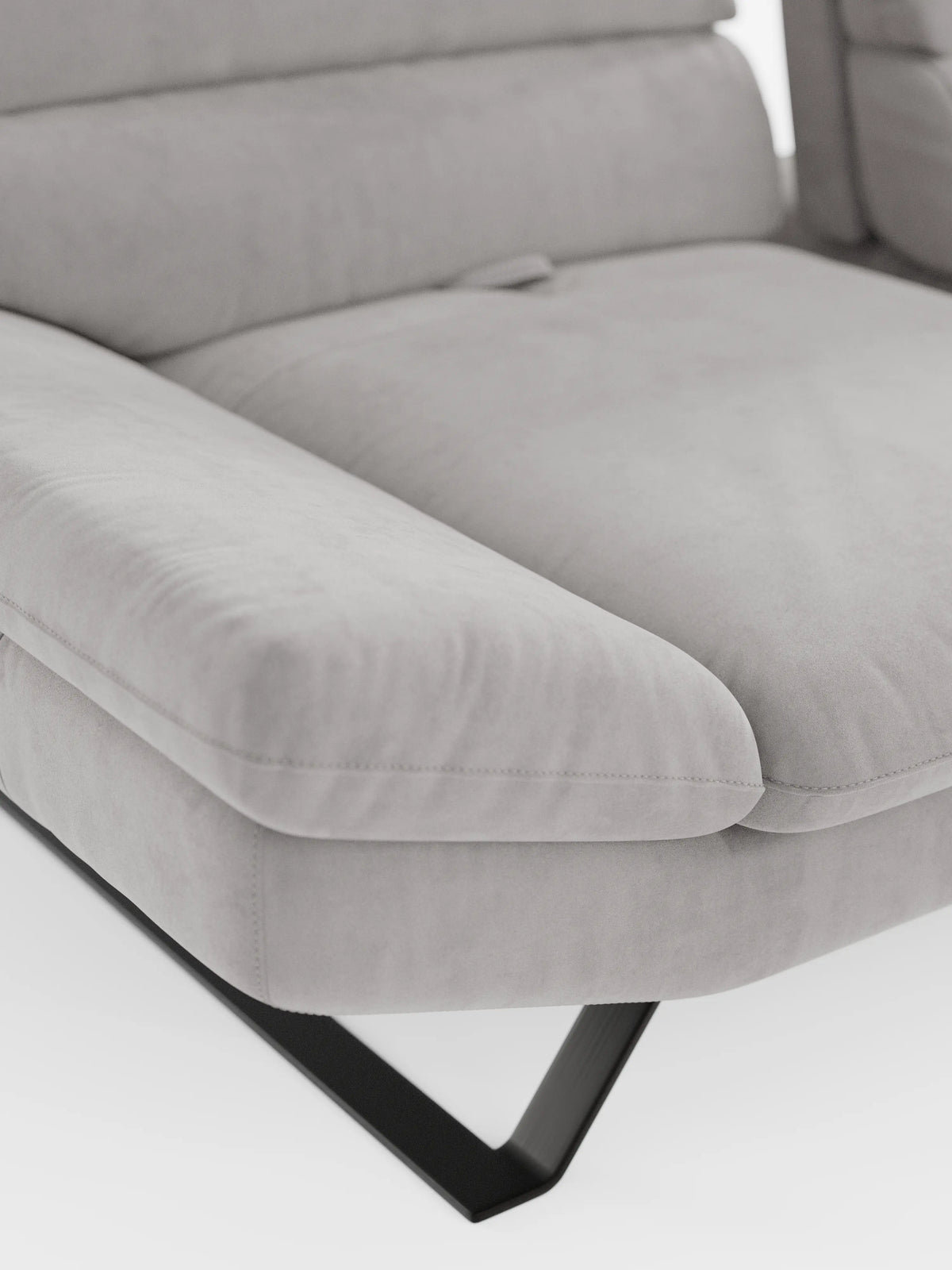 Primo piano del divano angolare Eclipse con penisola e schienali traslanti di Divani.Store, presentato in colore grigio chiaro, con rivestimento in morbida microfibra tecnica smacchiabile T11. La seduta presenta cuscini ampi e morbidi e gambe angolari in metallo nero su sfondo bianco. Sono visibili solo una parte dello schienale, con il suo elegante design traslante, la zona di seduta e un bracciolo.