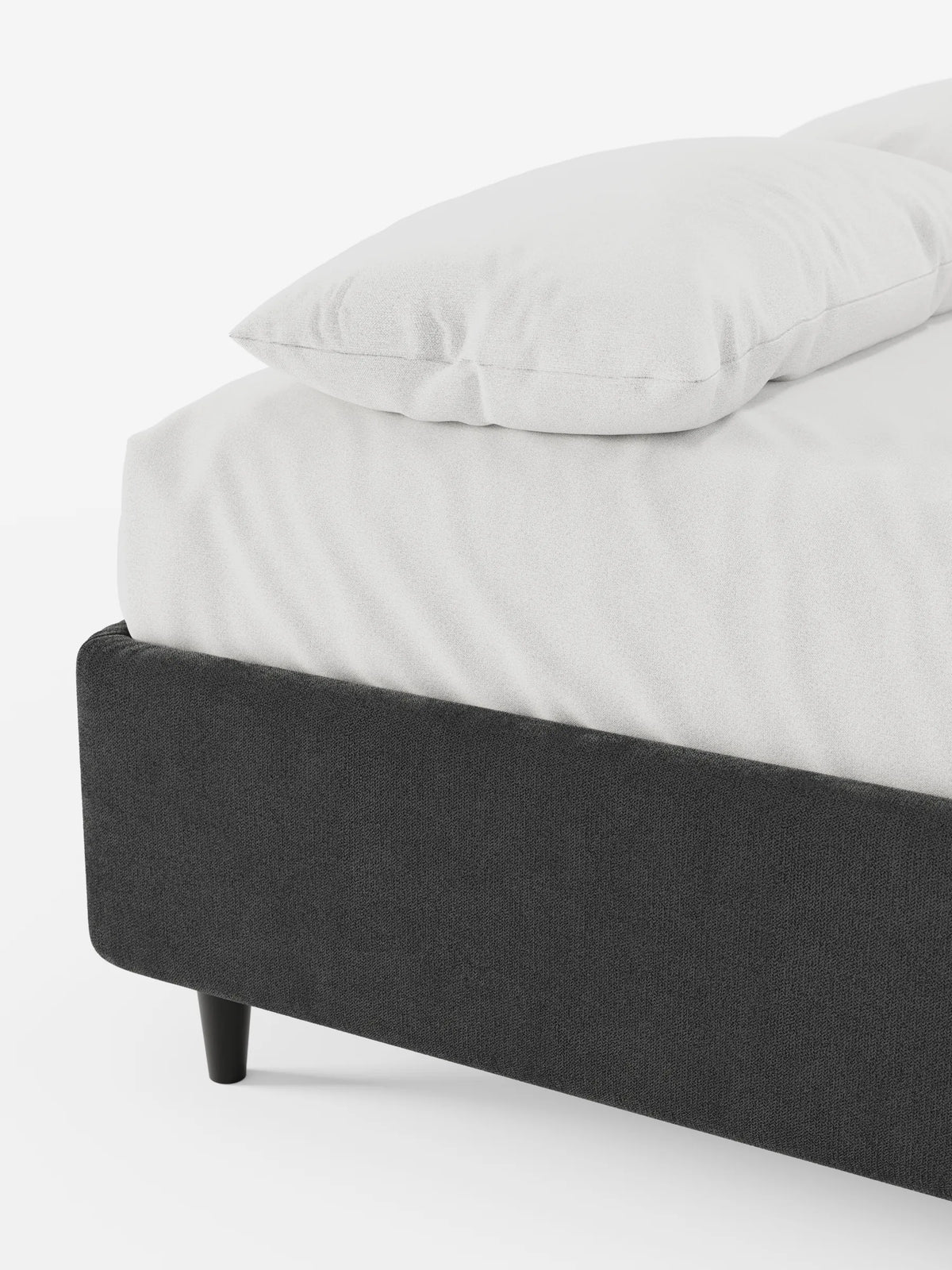 Un primo piano di un letto sommier ERON grigio scuro, imbottito e dotato di vano contenitore rivestito in tessuto impermeabile certificato Oeko-Tex, su gambe corte e coniche di colore scuro, con lenzuola bianche e un cuscino coordinato su uno sfondo bianco a tinta unita.