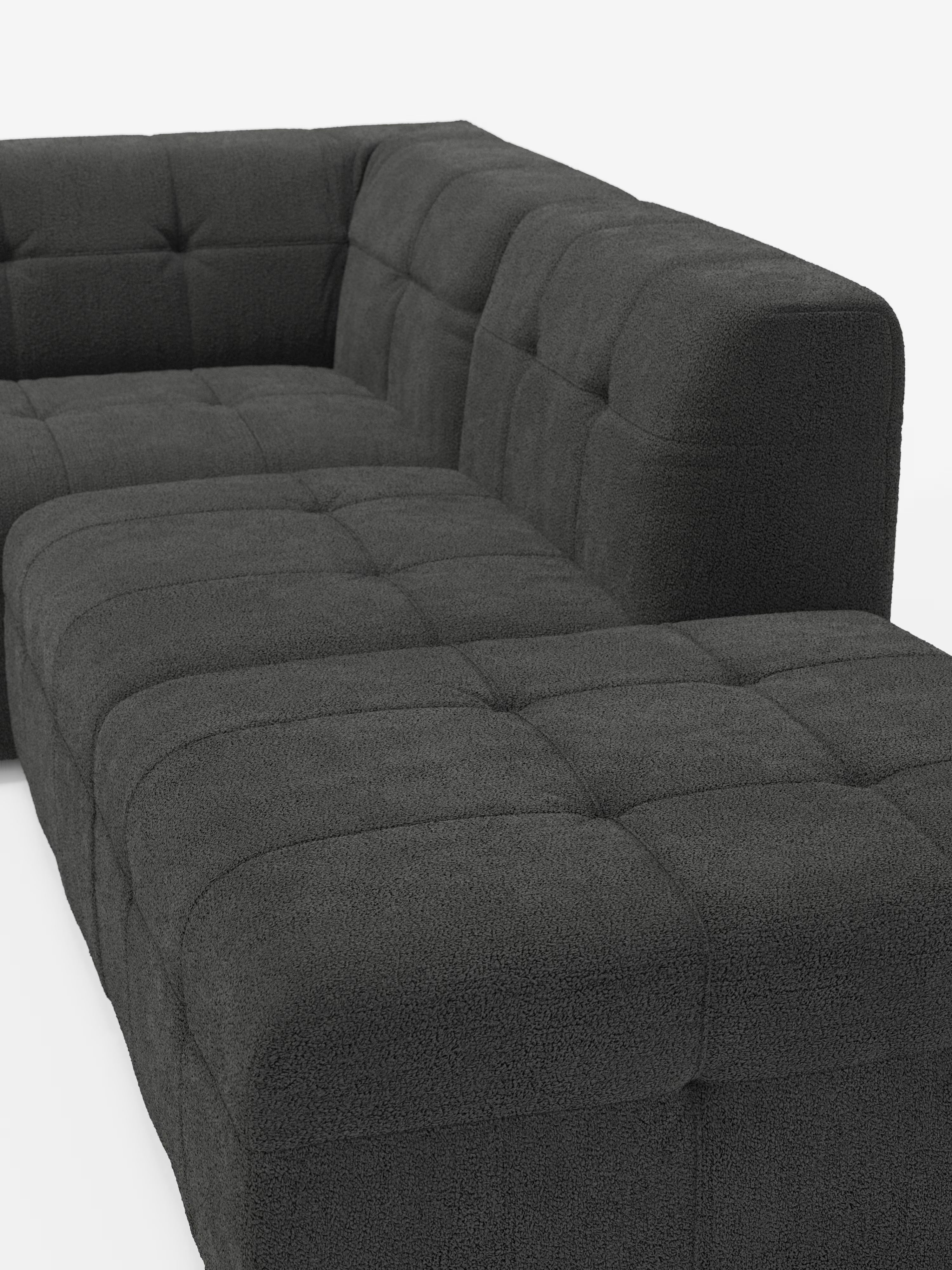 Un divano angolare componibile e modulare Mosaic in bouclé, dal colore grigio scuro e dallo stile contemporaneo, realizzato da Divani.Store, con chaise longue rivolta a destra. Rivestito in tessuto testurizzato T21 resistente alle macchie, questo divano presenta cuscini di seduta e schienale capitonné, braccioli bassi e squadrati e una silhouette pulita e squadrata che risalta su uno sfondo bianco a tinta unita.