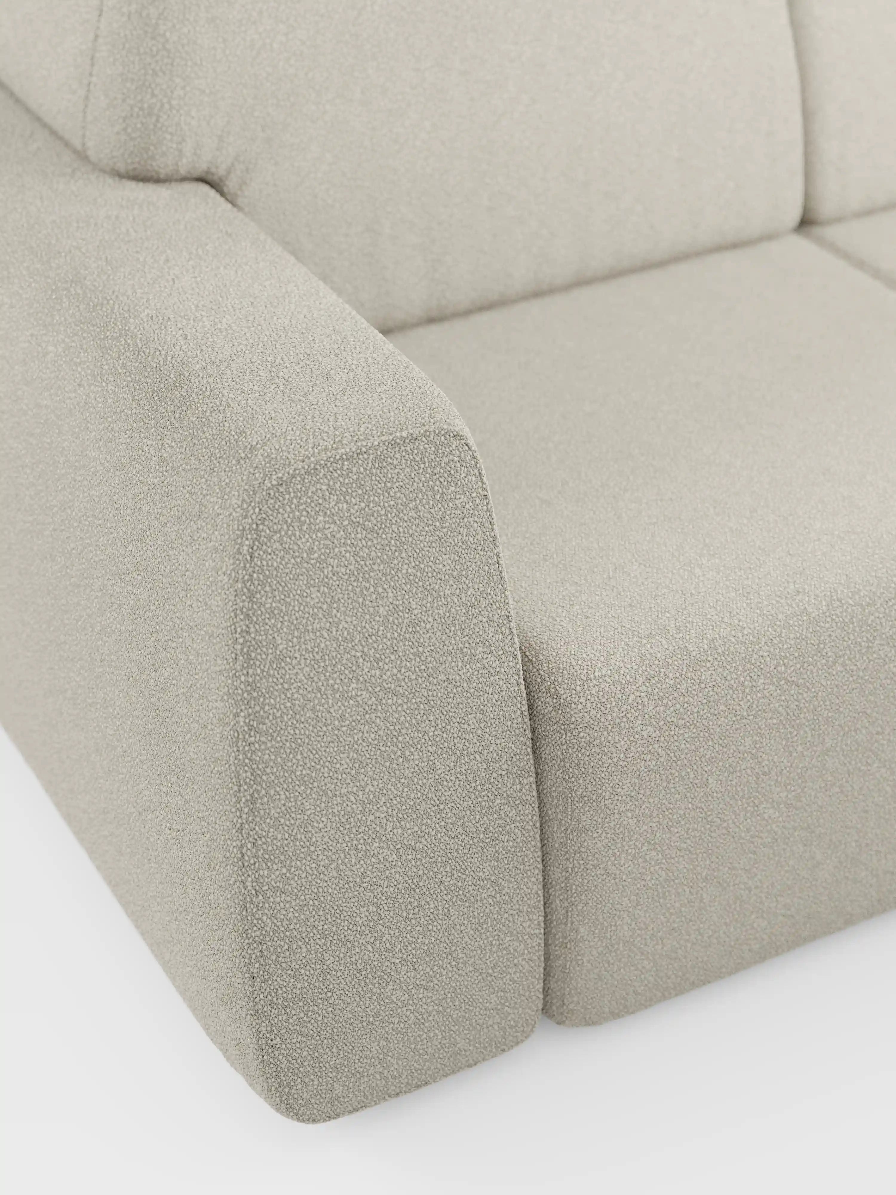 Primo piano del bracciolo e del cuscino di seduta del divano Orbit a 2 e 3 posti con sedute scorrevoli di Divani.Store, rivestito in tessuto smacchiabile effetto cotone T33 color beige chiaro. Il tessuto presenta una trama delicata e leggermente ruvida. Questo divano moderno, completamente sfoderabile, si caratterizza per le linee pulite e il design moderno e minimalista. Lo sfondo è a tinta unita e bianco.