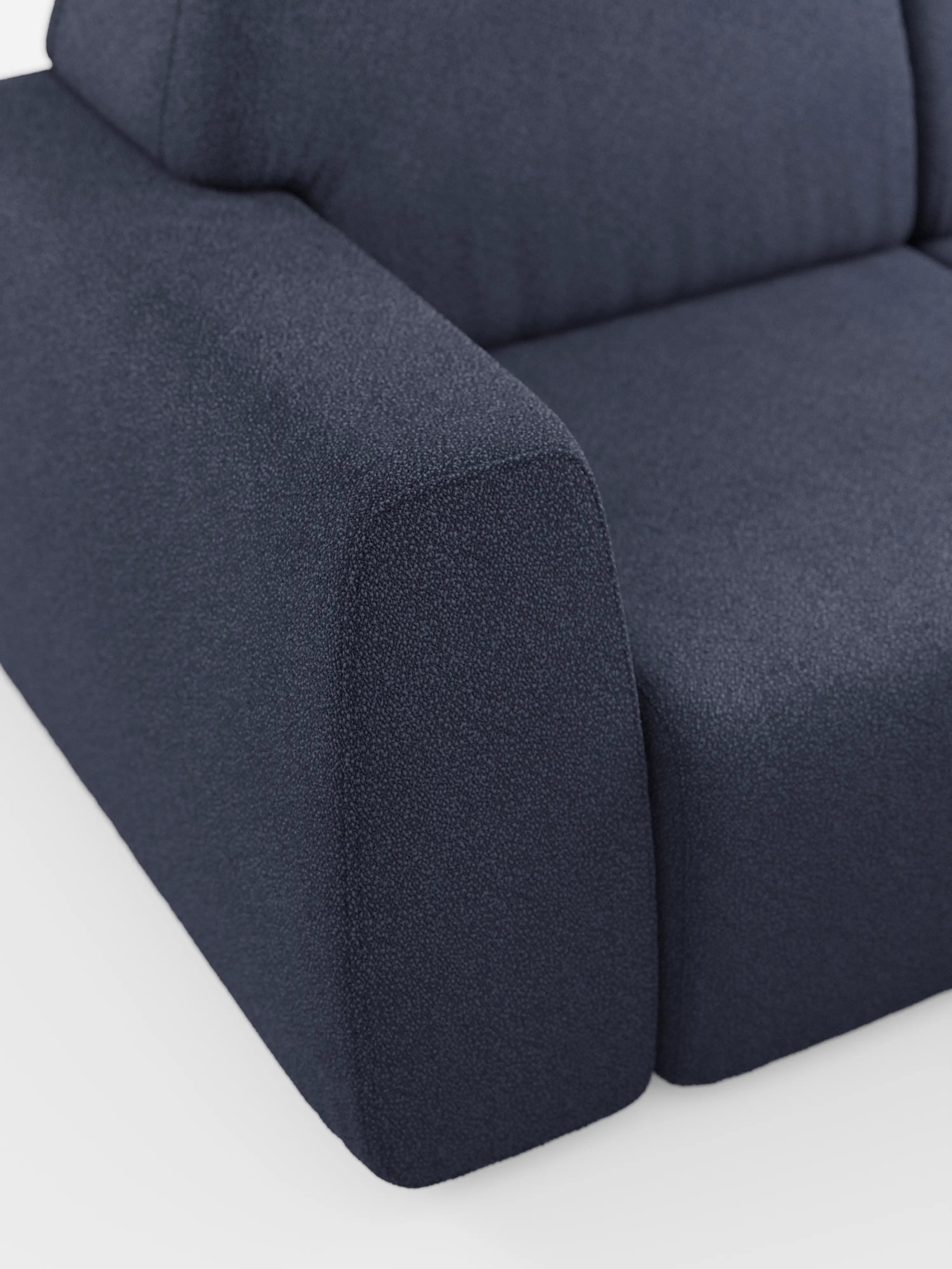 Primo piano dell'angolo del divano angolare Orbit con penisola reversibile e tutte le sedute allungabili in tessuto smacchiabile effetto cotone T33 di Divani.Modello in blu scuro, che mette in risalto il tessuto testurizzato effetto cotone antimacchia, l’ampio bracciolo, il cuscino di seduta e parte dello schienale, il tutto su uno sfondo bianco a tinta unita.
