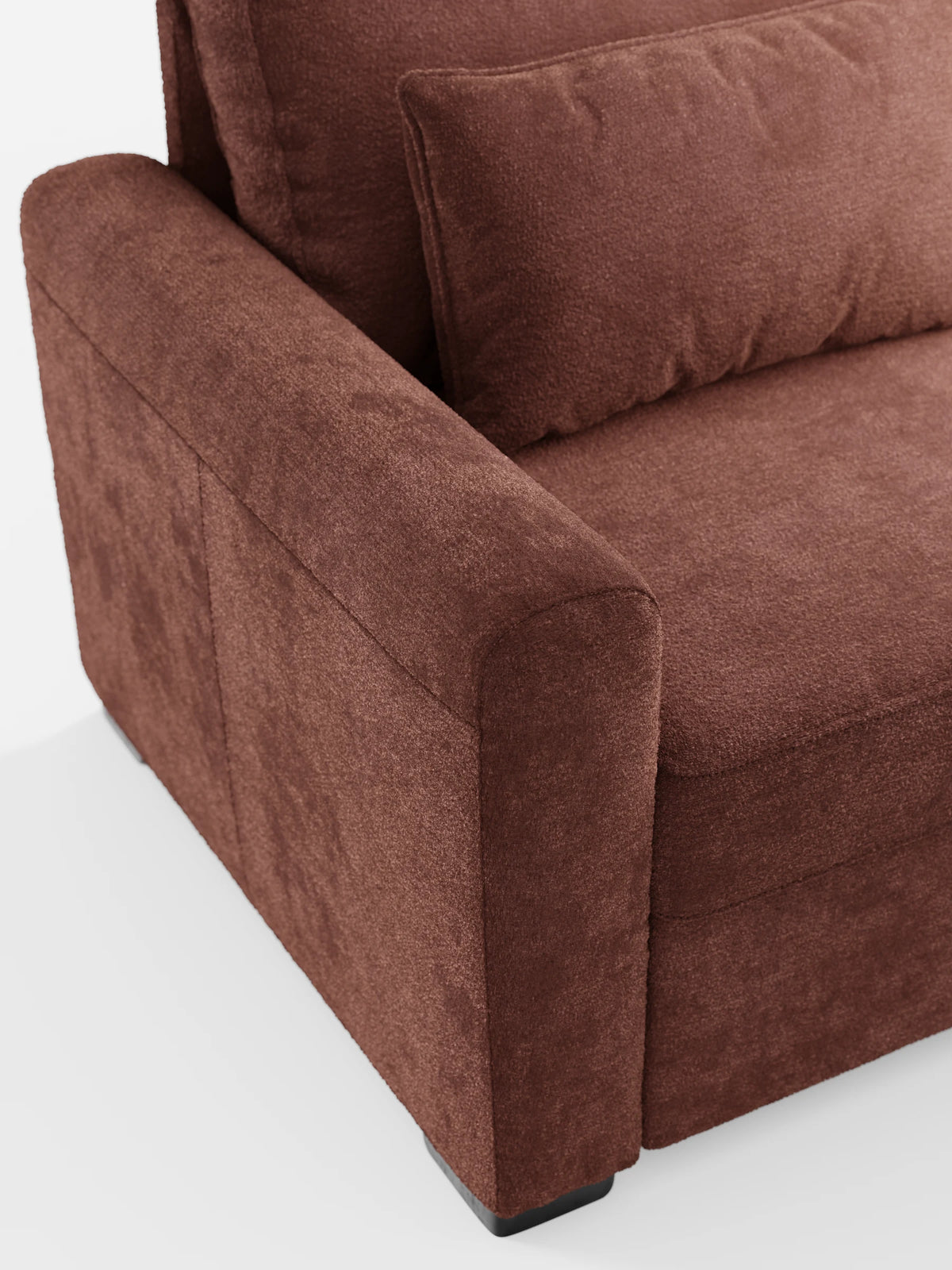 Un primo piano di un divano letto Ottaviano marrone con finitura in tessuto e letto estraibile – penisola reversibile e contenitore in tessuto materico lavabile – che mette in risalto il bracciolo arrotondato e un cuscino decorativo abbinato su uno sfondo chiaro a tinta unita.