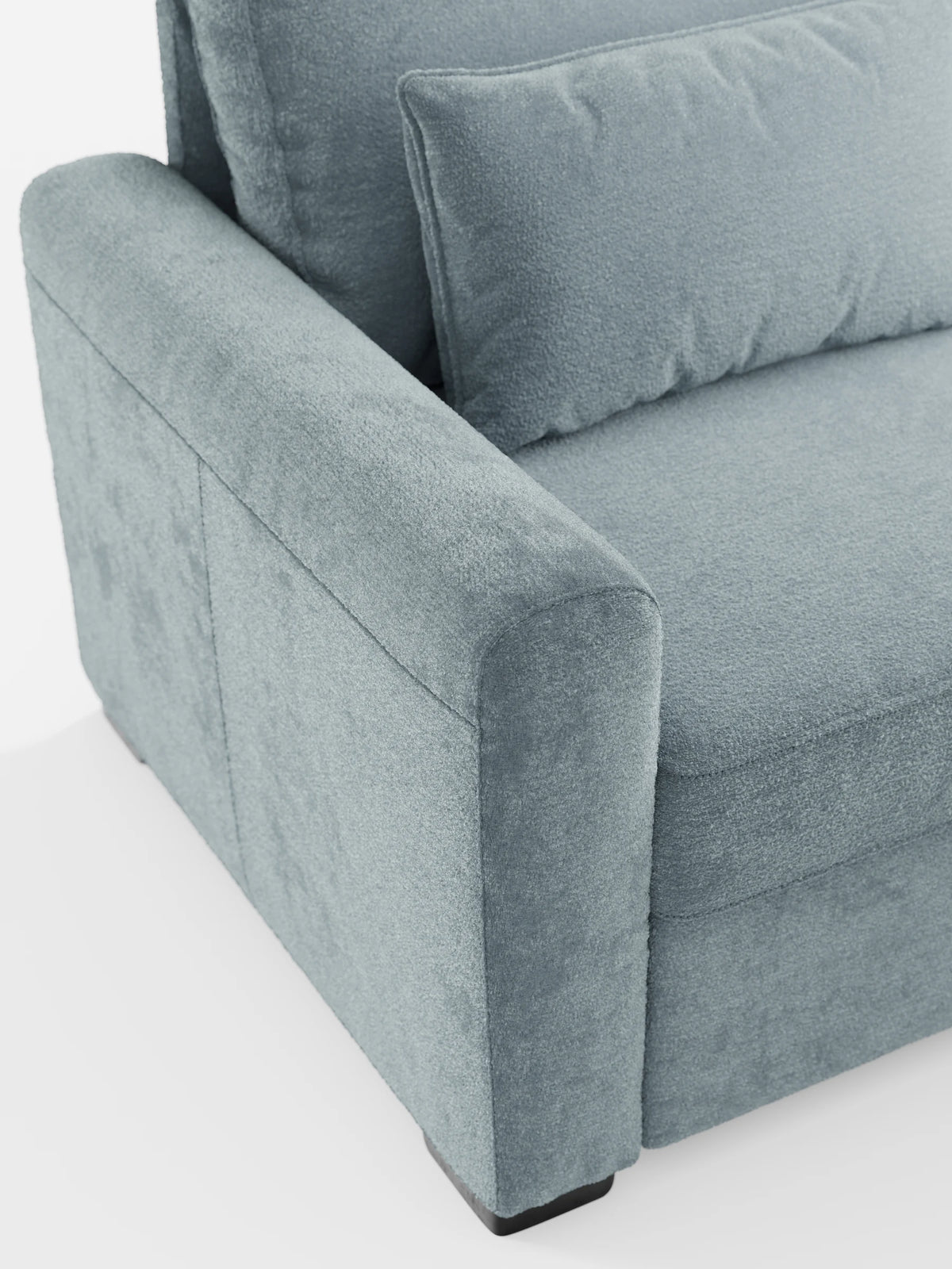 Un primo piano del divano letto Ottaviano con letto estraibile - penisola reversibile e contenitore in tessuto materico smacchiabile, con braccioli rivestiti in tessuto materico blu ardesia, cuscino decorativo abbinato e gambe in legno scuro.