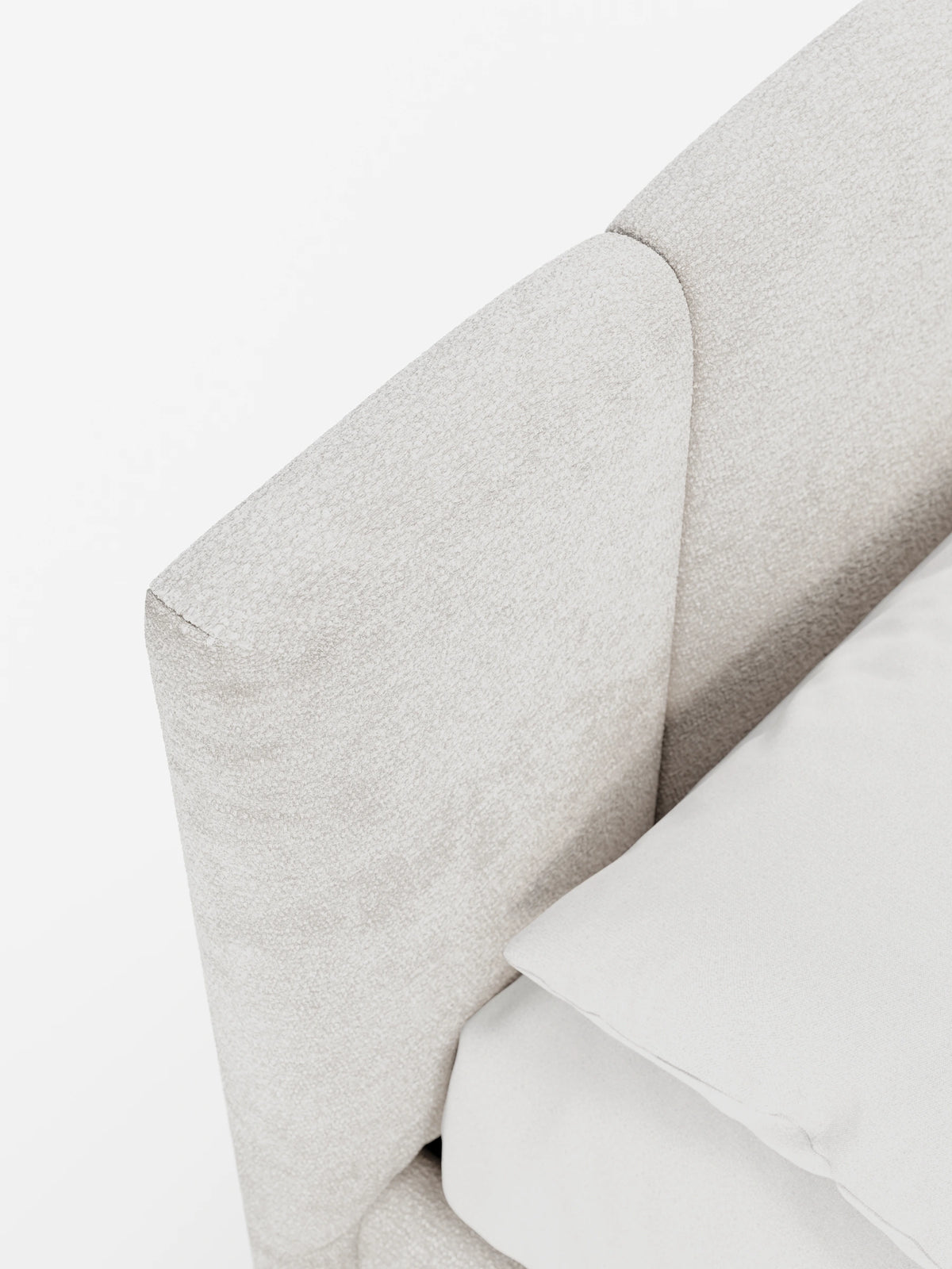 Un primo piano di un letto imbottito ARKAM con contenitore e testiera a lavorazione verticale, caratterizzato da una testiera rivestita in beige chiaro con cuciture verticali e un cuscino liscio di tonalità più chiara, sullo sfondo di una parete bianca brillante.