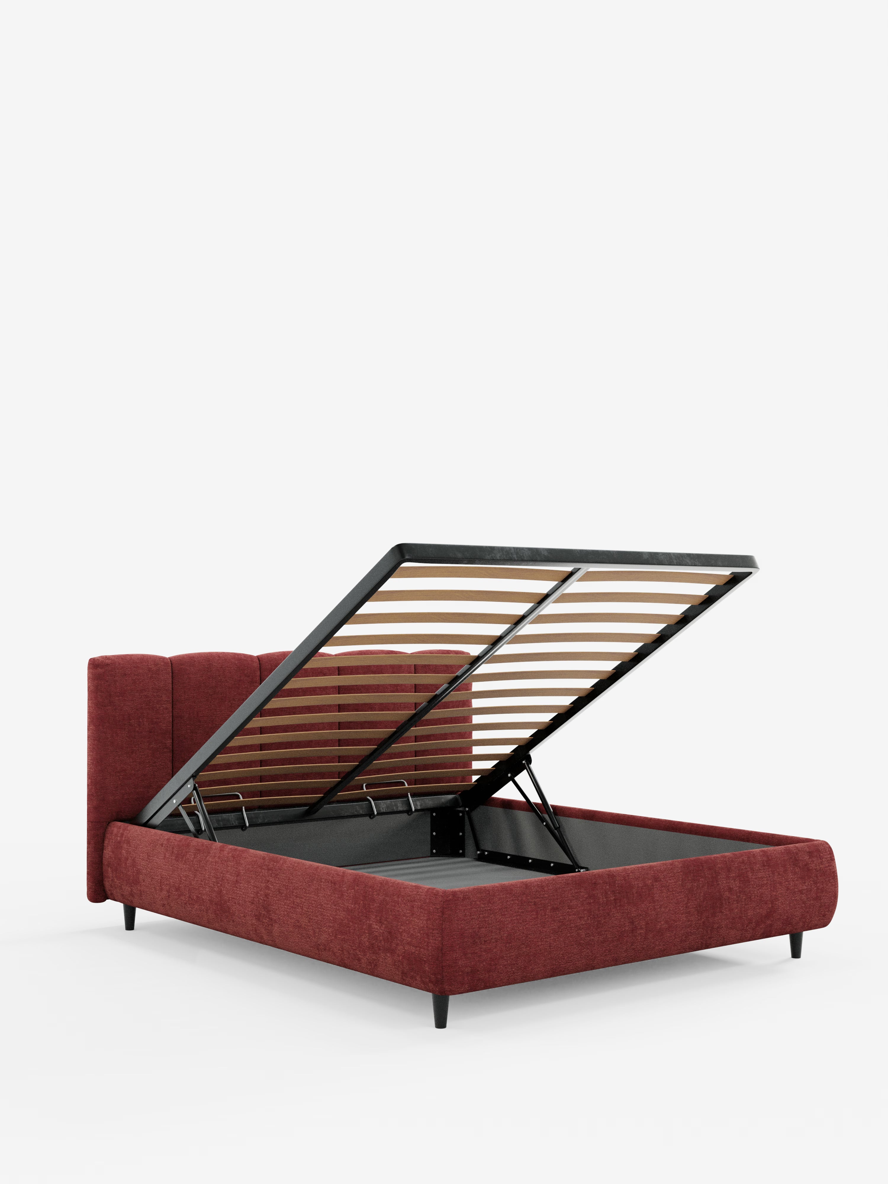 Un letto imbottito ARKAM in stile shabby chic con contenitore di Letti.store, rivestito in tessuto rosso intenso certificato Oeko-Tex® con una testiera alta e imbottita, cucita verticalmente. La struttura si solleva per rivelare un ampio vano contenitore sottostante, sostenuto da doghe in metallo e legno con bracci idraulici. Presentato su uno sfondo bianco a tinta unita.