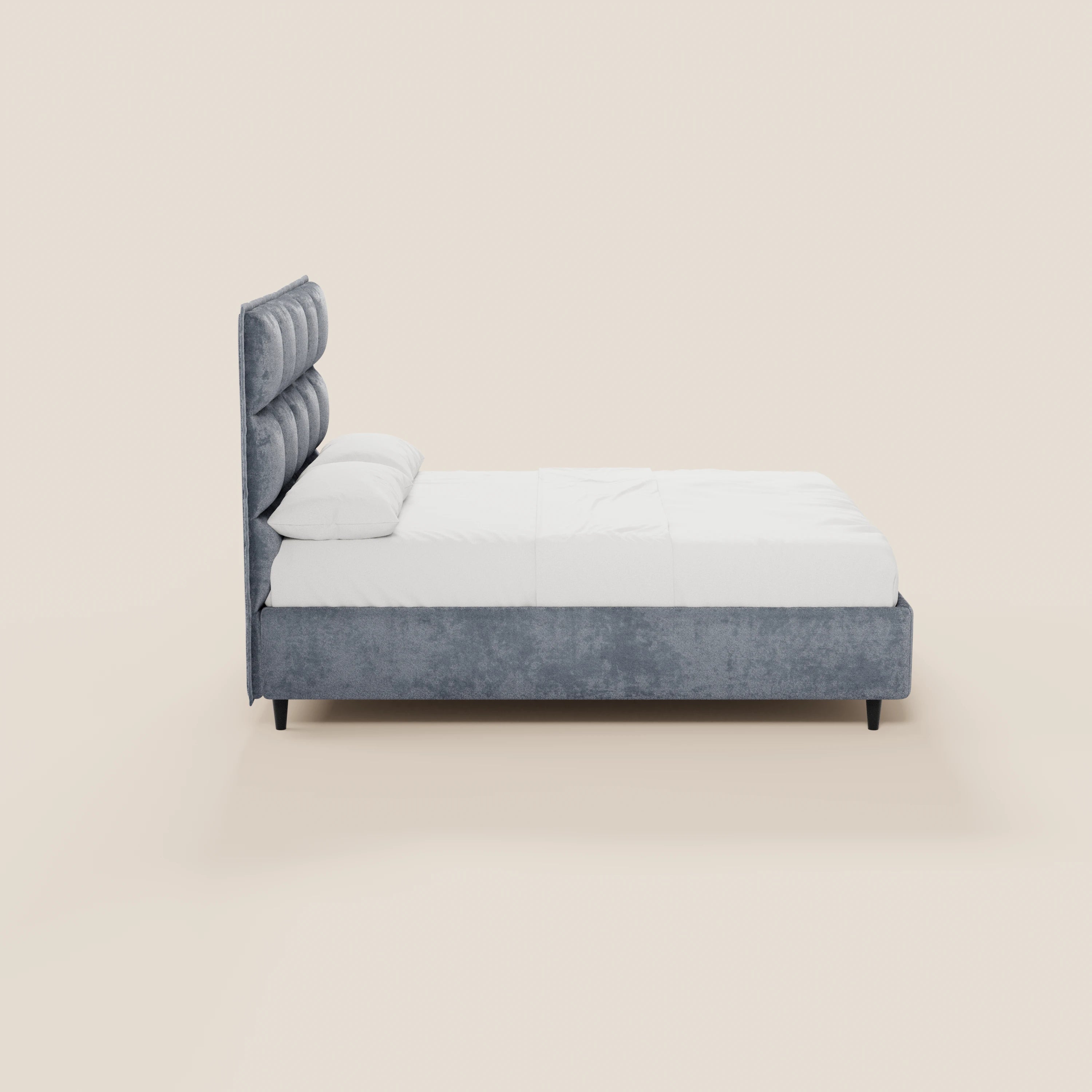 Una vista laterale del letto imbottito AURO di Letti.store mostra una testiera alta, capitonné in ciniglia certificata Oeko-Tex®, biancheria da letto bianca con due cuscini, gambe corte nere, il tutto su uno sfondo beige chiaro.